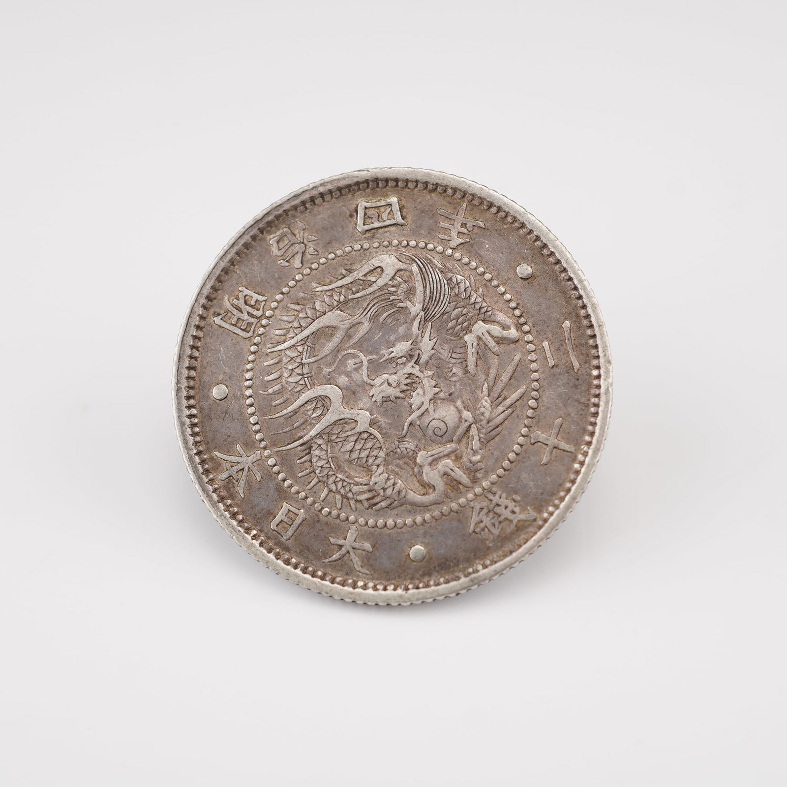 1871 Meiji Era 5 Sen Coin: This silver coin was struck during the early Meiji era and features a detailed dragon encircled by beaded borders on the obverse along with inscriptions in Japanese characters. The reverse displays a 