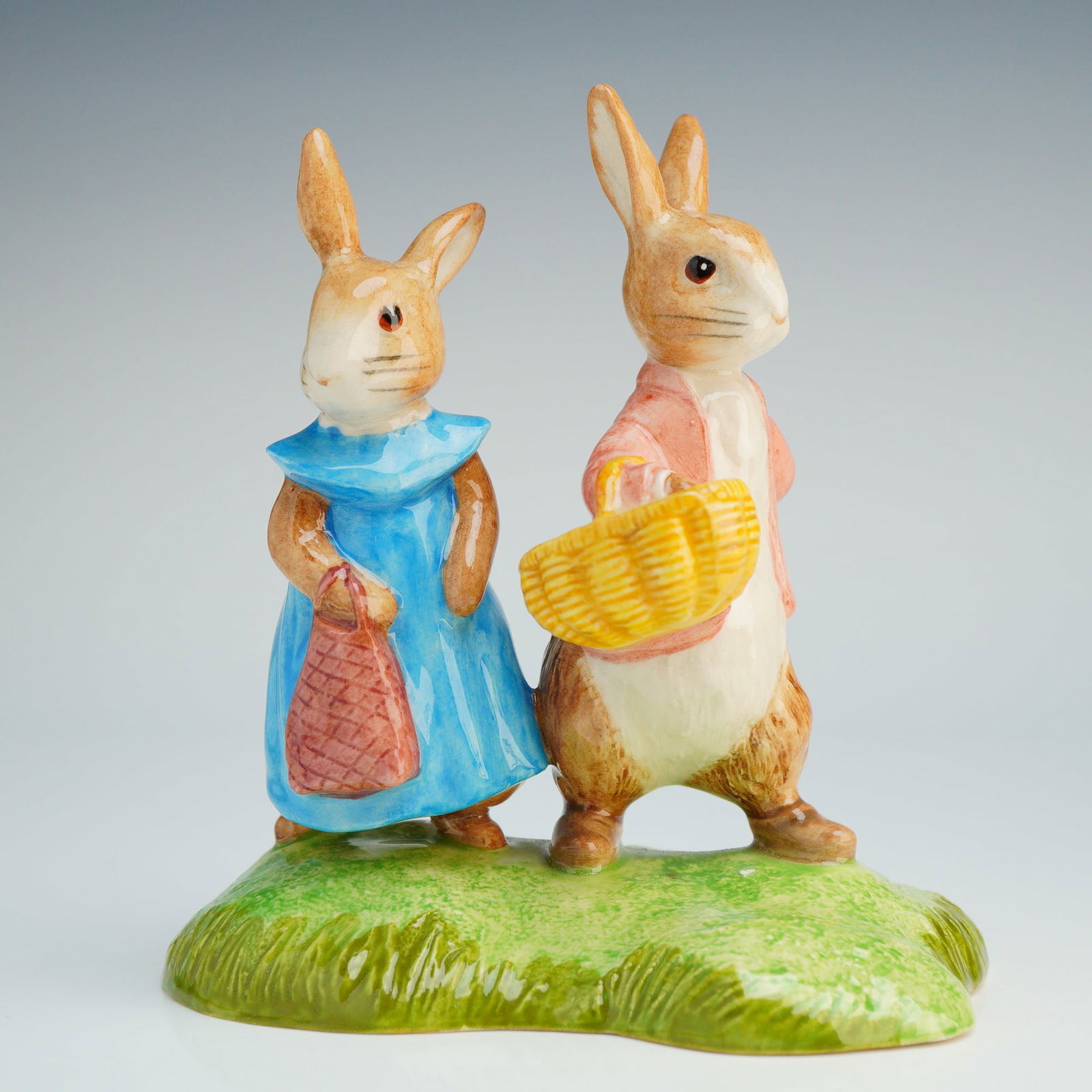 Beswick Beatrix Potter Tableau ,Flopsy and Benjamin Bunny P4155: This hand-made and hand-decorated tableau depicts two rabbits standing on a molded green grassy base. One figure is depicted in a blue dress with a red patterned bag, while the other wears a pink jack