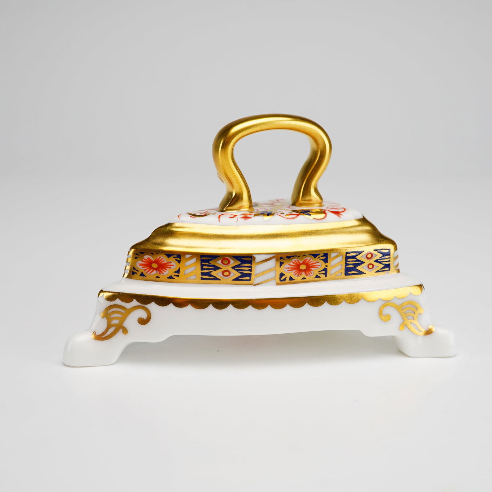 Royal Crown Derby Bone China Imari Paperweight, Iron on Stand: A Royal Crown Derby fine bone China paperweight modeled as a miniature flat iron resting on a footed base. The piece is decorated in the Traditional Imari pattern with red, blue, and gold floral and g