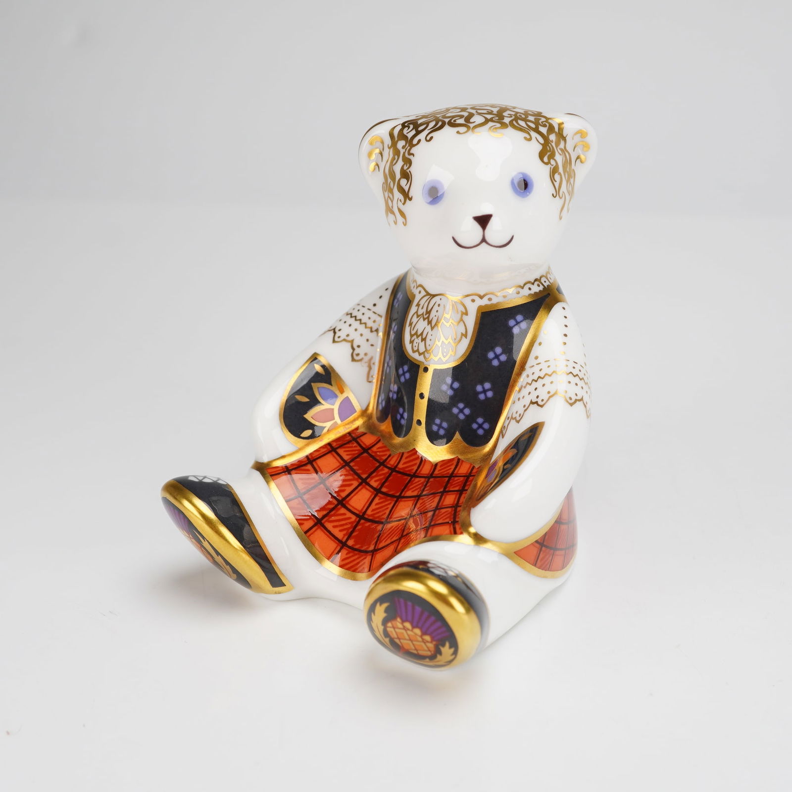 Royal Crown Derby Bone China Paperweight, Shona: A Royal Crown Derby fine bone china paperweight titled Shona from the Scottish Teddy series. This seated bear figural paperweight is decorated in an Imari-inspired palette with 22-karat gold gilding.