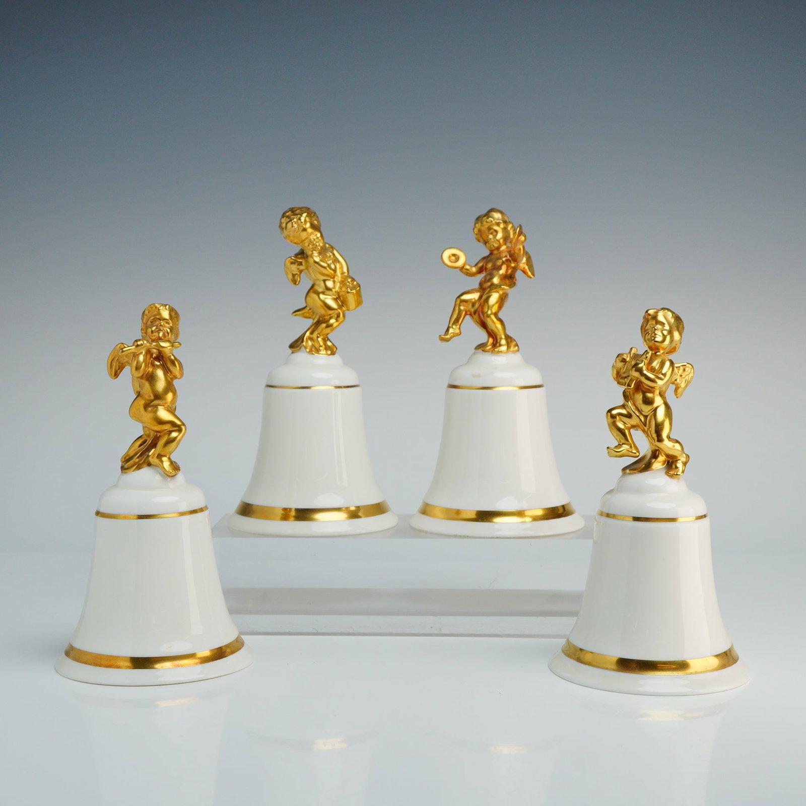 4pc Royal Doulton Bone China Bells, The Speech of Angels Limited Edition: Each bell features a white glazed body with gilded banding at the base and a handle cast in the form of a detailed, gilded cherub playing various musical instruments, including cymbals and a flute. Th