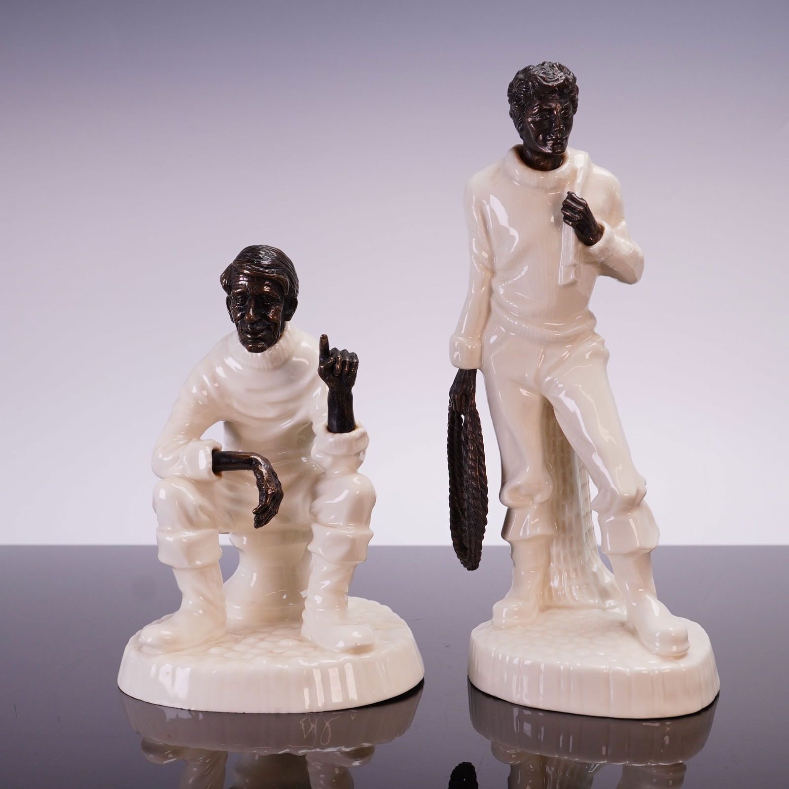 2pc Minton Bone China and Bronze Figurines, Fisherman and Travelers Tales: This 2pc set of Minton mixed-media figurines consists of the models titled Travelers Tales MS01 and The Fisherman MS13. Each figurine is crafted from fine bone china and dark-patinated bronze. The fig