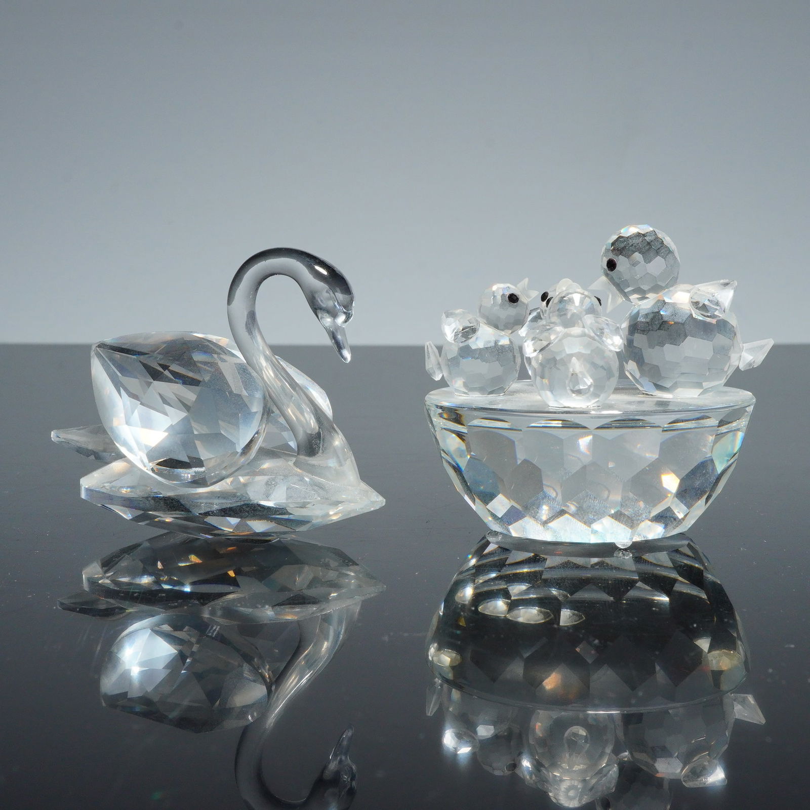 2pc Swarovski Crystal Figurines, Swan and Bird Bath: A collection of two Swarovski crystal figurines, comprising a swan and a bird bath with cygnets. Each piece is constructed from multi-faceted lead crystal. The swan figurine features a smooth, slender