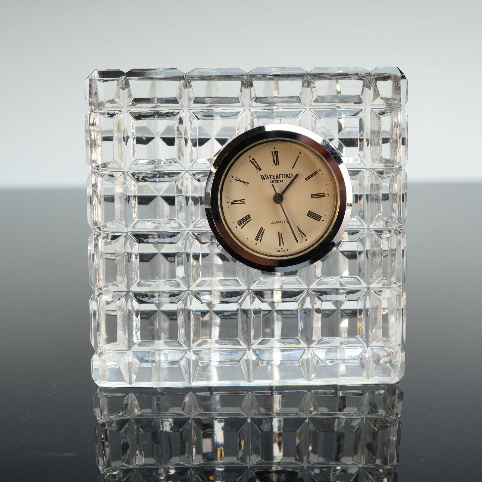 Waterford Crystal Offset Desk Clock: A Waterford crystal featuring a square clear crystal housing with a deeply cut geometric grid design. The piece contains a centrally inset round silver-tone quartz clock movement with an off-white fac