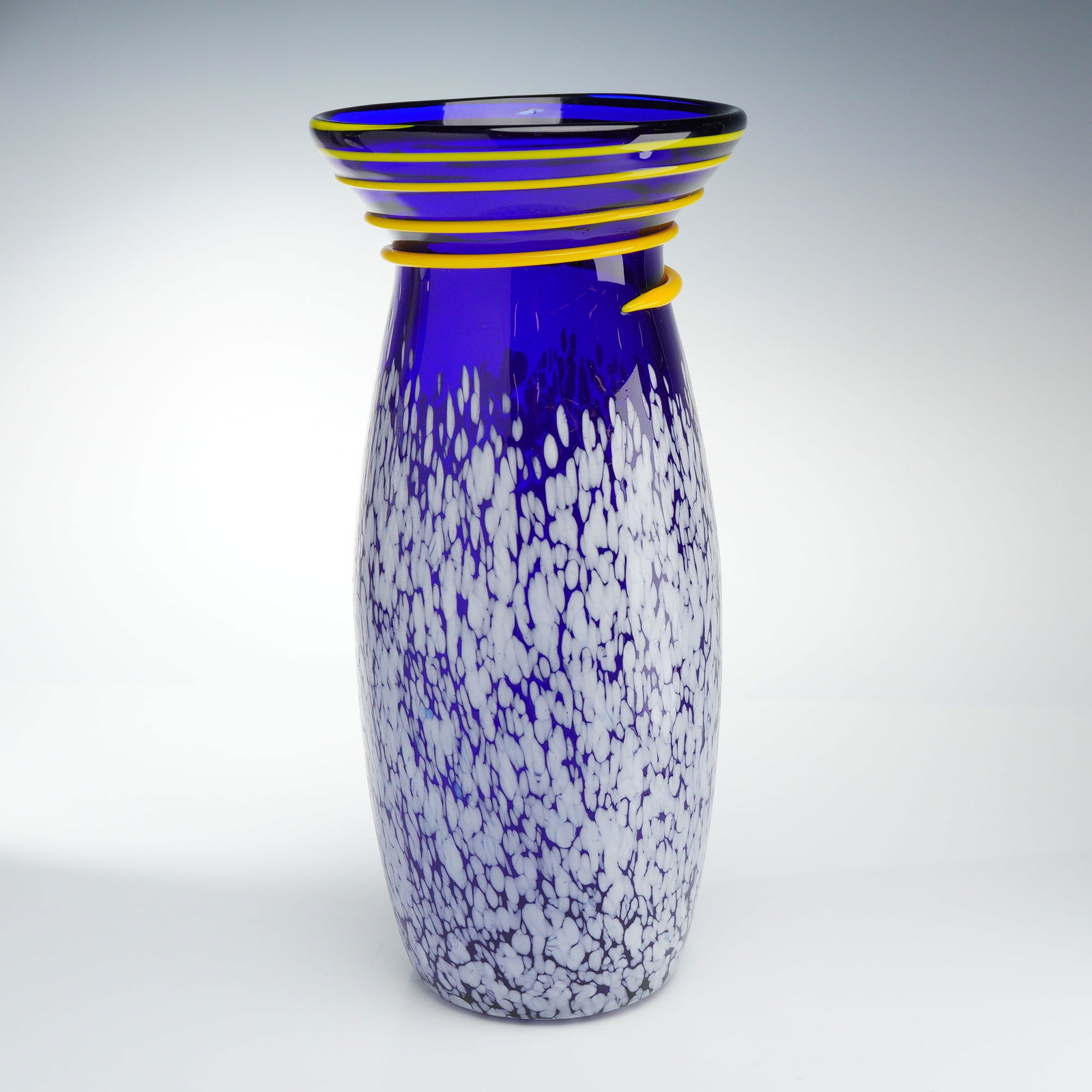 Contemporary Hand-Blown Cobalt Art Glass Vase with Yellow Spiral Trail: A contemporary hand-blown studio art glass vase featuring a tapered ovoid body in vibrant cobalt blue. The lower portion of the vessel is decorated with a mottled white frit pattern, creating a