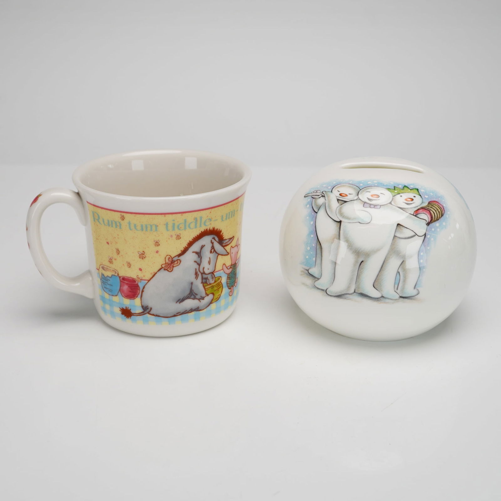 2pc Royal Doulton Collectibles Disney Pooh Mug & Snowman Money Bank: Two ceramic items manufactured by Royal Doulton. The first is a mug from the Winnie the Pooh Gift Collection, hand-decorated with characters including Winnie the Pooh, Tigger, Eeyore, and Piglet. The