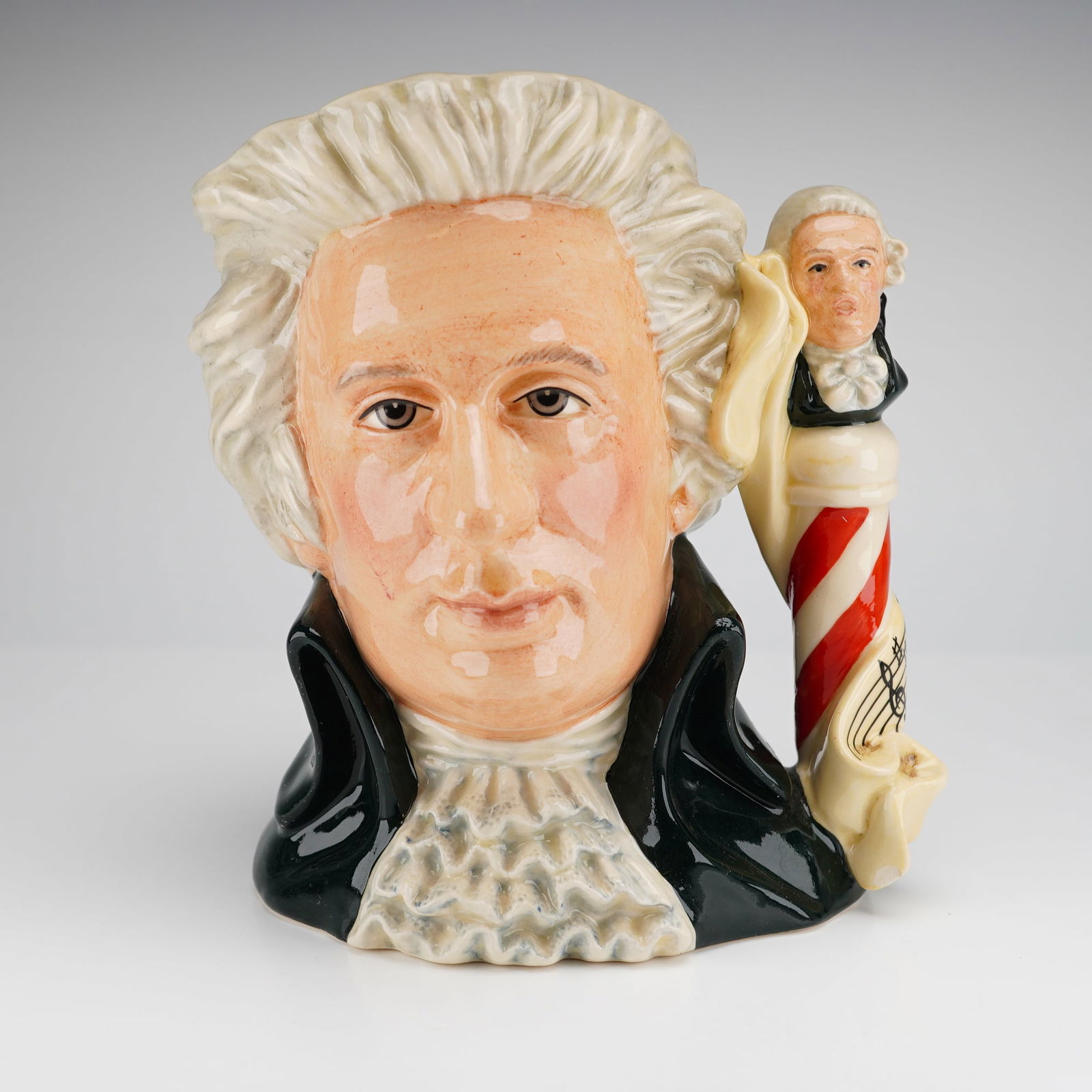Royal Doulton Character Jug D7031 Mozart Large: This Royal Doulton character jug, model D7031, is titled Mozart and was modeled by Stanley James Taylor. The hand-decorated ceramic piece is finished with a high-gloss glaze. The jug portrays Wolfgang