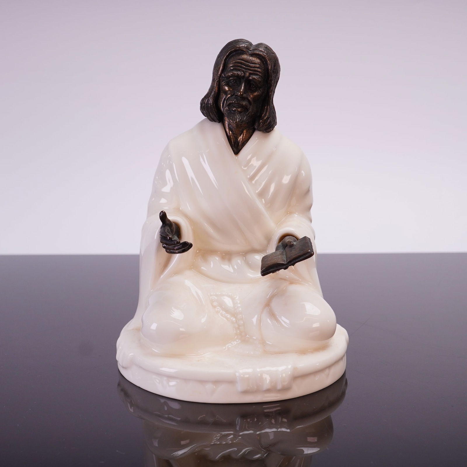 Minton Fine Bone China and Bronze Figurine The Sage MS25: A Minton fine bone china and bronze figurine titled The Sage, model number MS25, manufactured in England circa 1978. The piece depicts a seated male figure in a cross-legged position, wearing robes wi