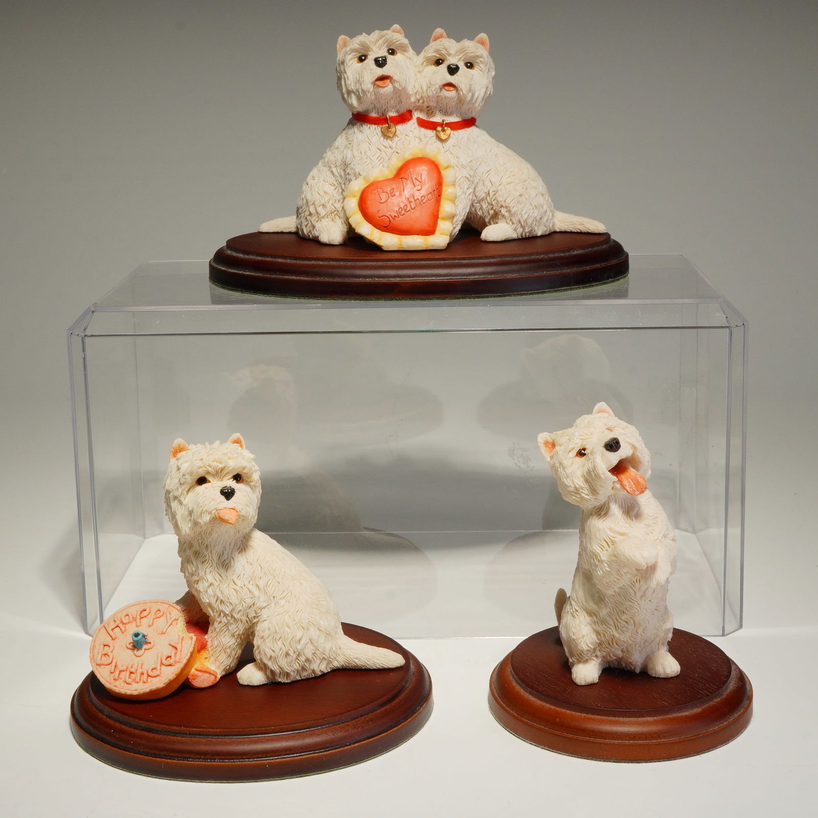 Three Sherratt & Simpson West Highland White Terrier Figurines with Bases: These hand-painted pieces feature realistic textural detailing of the breed's white coat. The group includes a pair of dogs adorned with red collars and a heart inscribed Be My Sweetheart, a single do