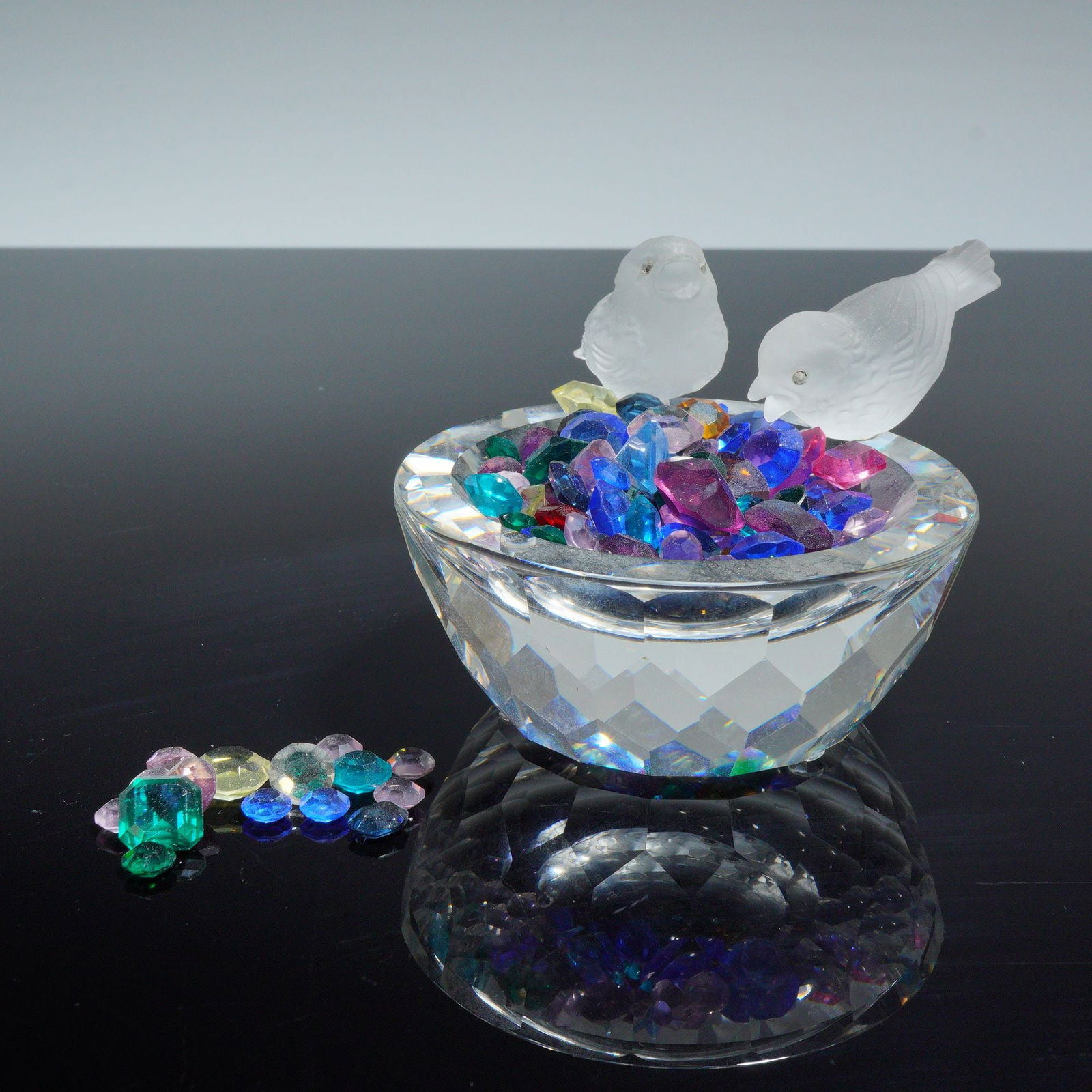 Swarovski Crystal Figurine, Bird Bath 010029: Featuring a faceted clear crystal bowl with two frosted crystal bird figurines perched on the rim. The bowl is accompanied by a collection of loose colored crystals in various faceted shapes and hues,