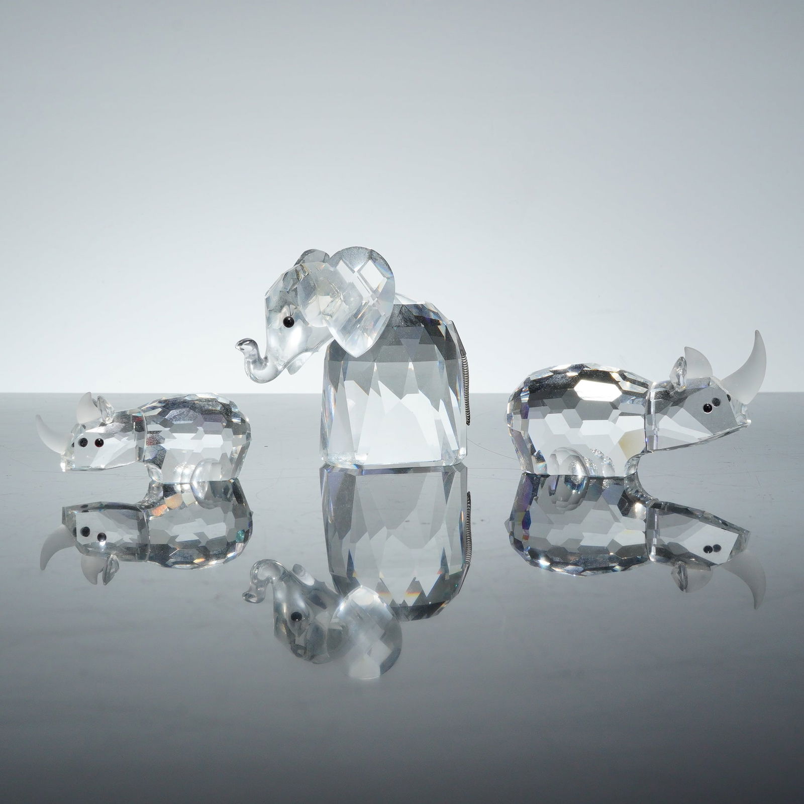 3pc Swarovski Crystal Figurines, Mother & Baby Rhinoceros and Elephant: A group of three Swarovski faceted clear lead crystal figurines comprising two rhinoceroses, representing a mother and baby, and an elephant. These collectibles are constructed from multiple geometric