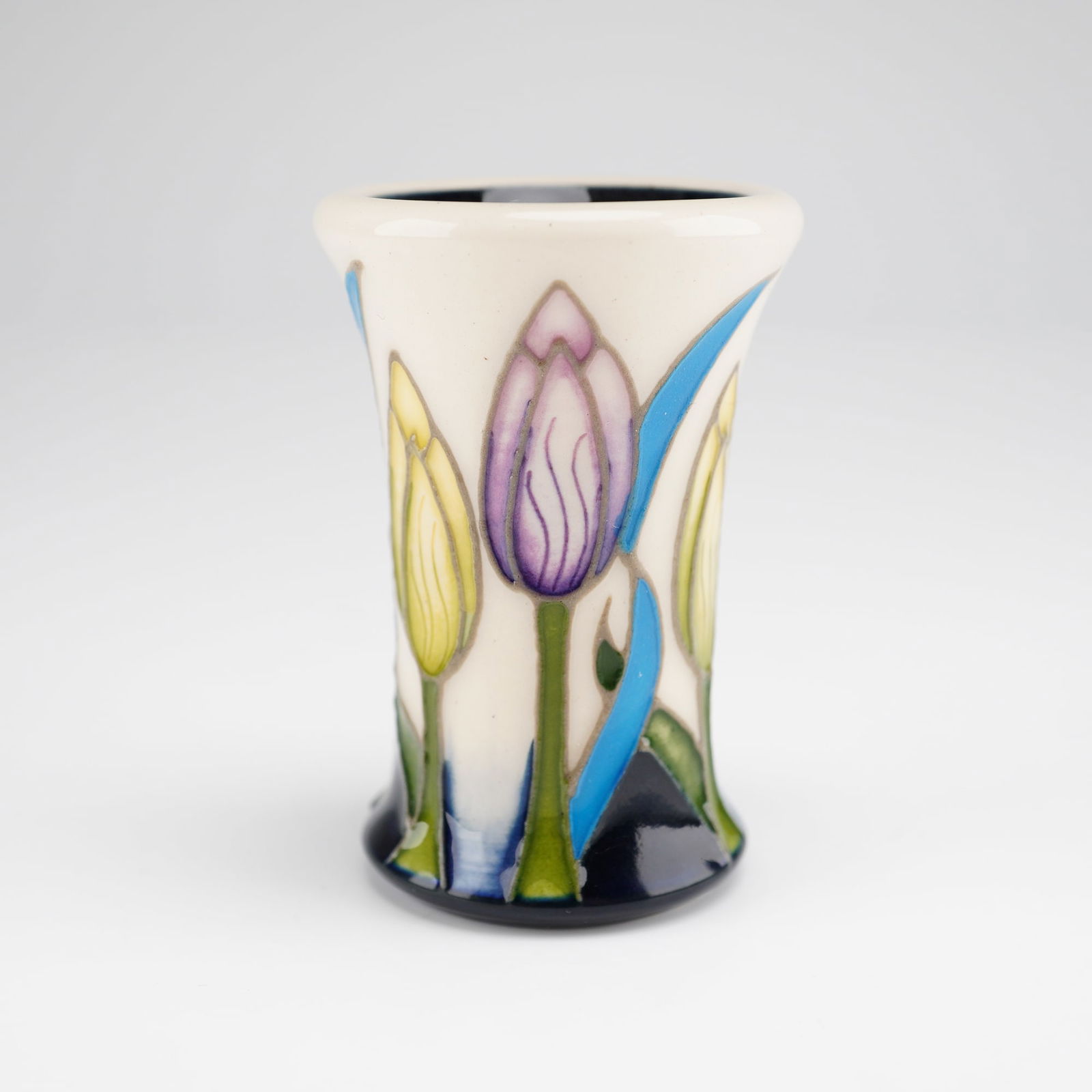 Moorcroft Mini Tulips Pottery Bud Vase: A Moorcroft mini vase in the Tulips pattern. This miniature pottery vessel features a flared rim and hand-painted tubelined decoration. The composition includes stylized purple and yellow tulip buds
