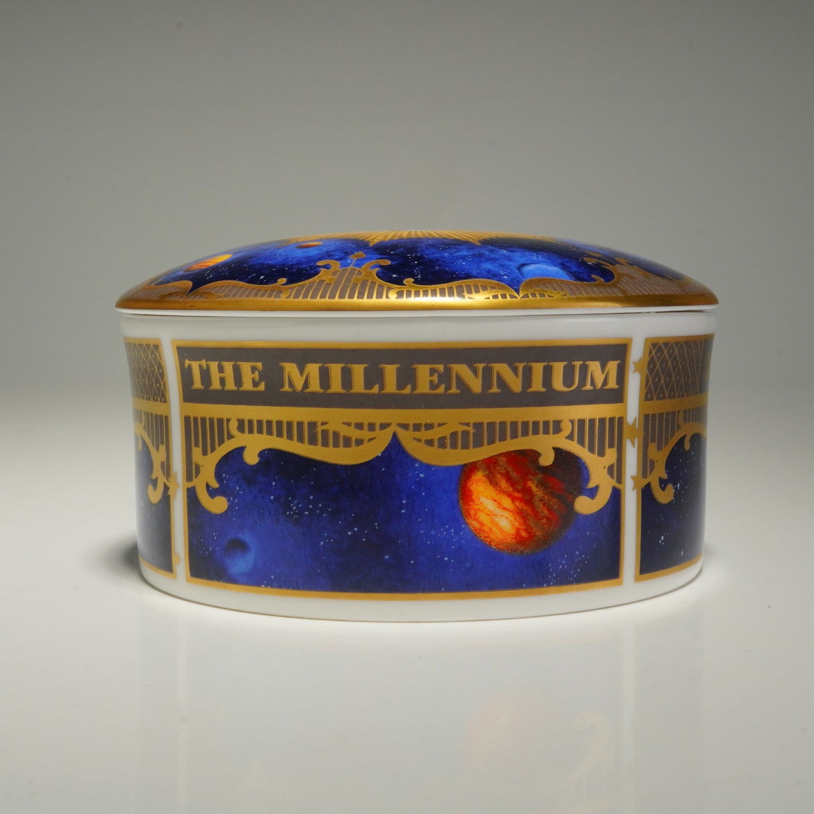 Royal Worcester Round Lidded Box, To Celebrate the Millennium: A Royal Worcester fine bone china round lidded box titled To Celebrate the Millennium. The exterior features a celestial design depicting various planets and stars against a deep blue ground, framed