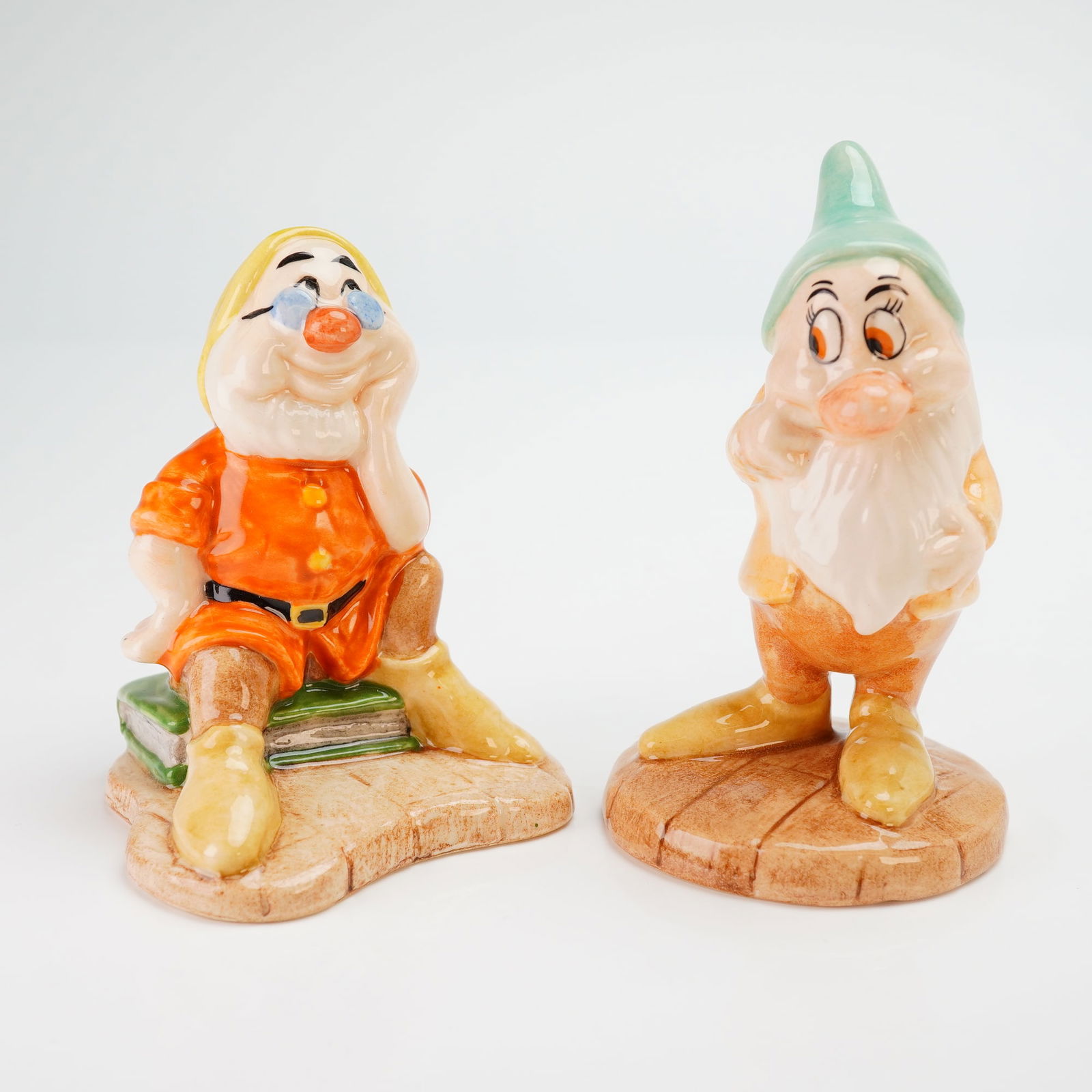 2pc Royal Doulton Disney Snow White Figurines, Bashful SW16 & Doc SW10: This lot features two hand-painted, glazed figurines from the Royal Doulton Walt Disney's Classic Snow White and the Seven Dwarfs collection, specifically depicting the characters Doc and Bashful. Doc