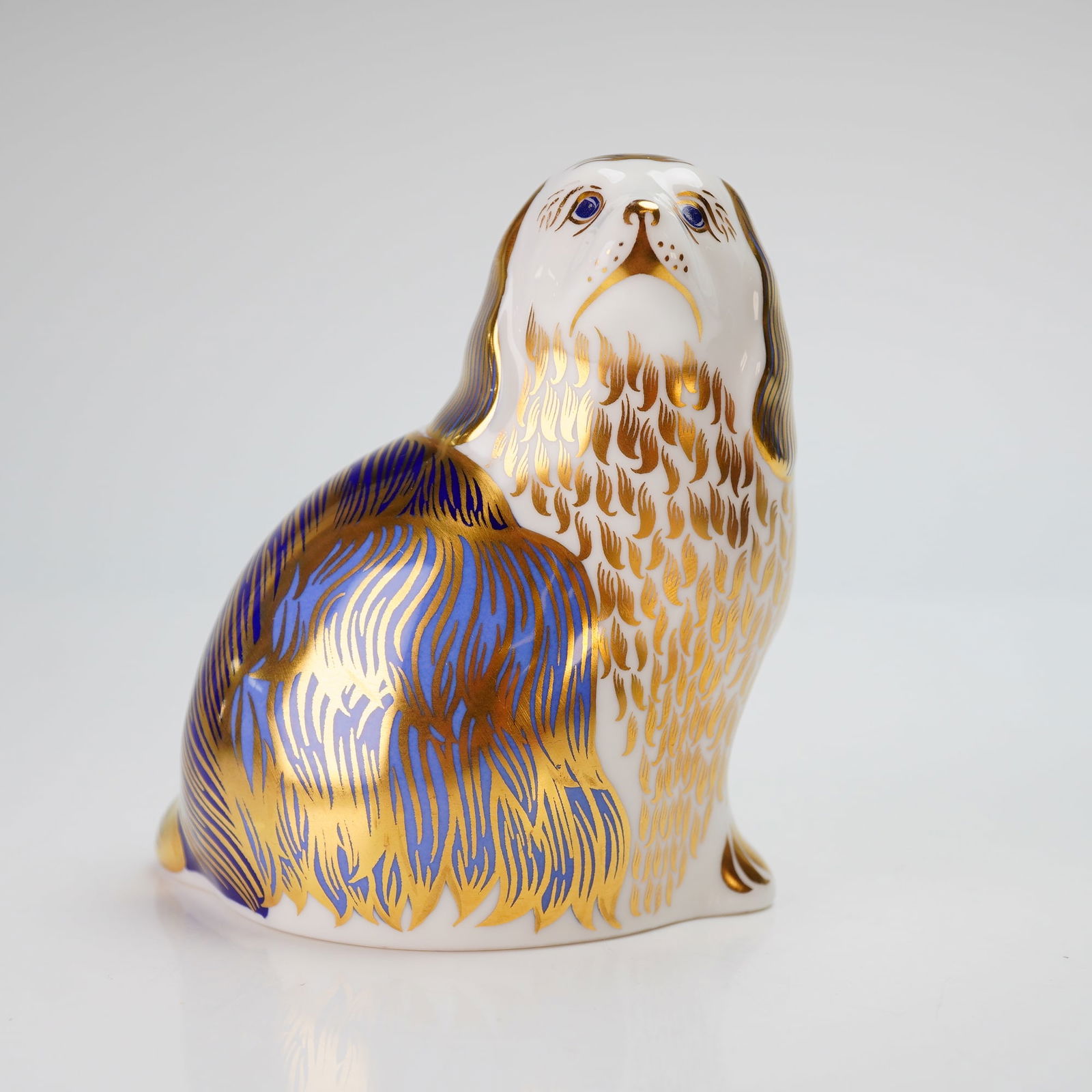 Royal Crown Derby Paperweight, King Charles Spaniel: This fine bone china figurine is modeled as a seated dog and decorated in the traditional Imari palette of cobalt blue and white with extensive 22kt gold gilding. The stylized representation of a long