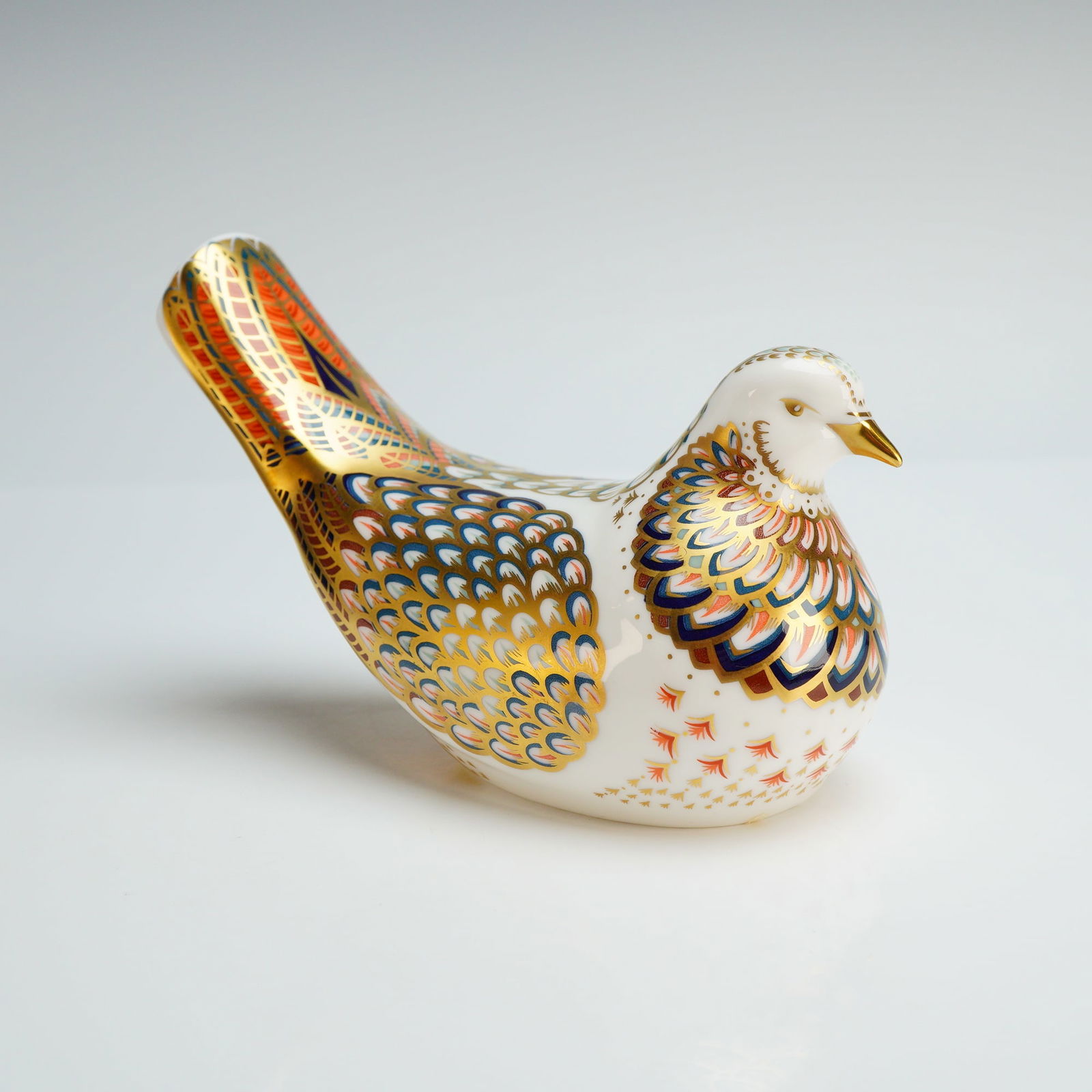 Royal Crown Derby Paperweight, Turtle Dove: The figurine features an Imari-inspired design with polychrome accents in red, blue, and orange, finished with gold gilding. The underside bears the manufacturer's red backstamp, the Roman numeral yea