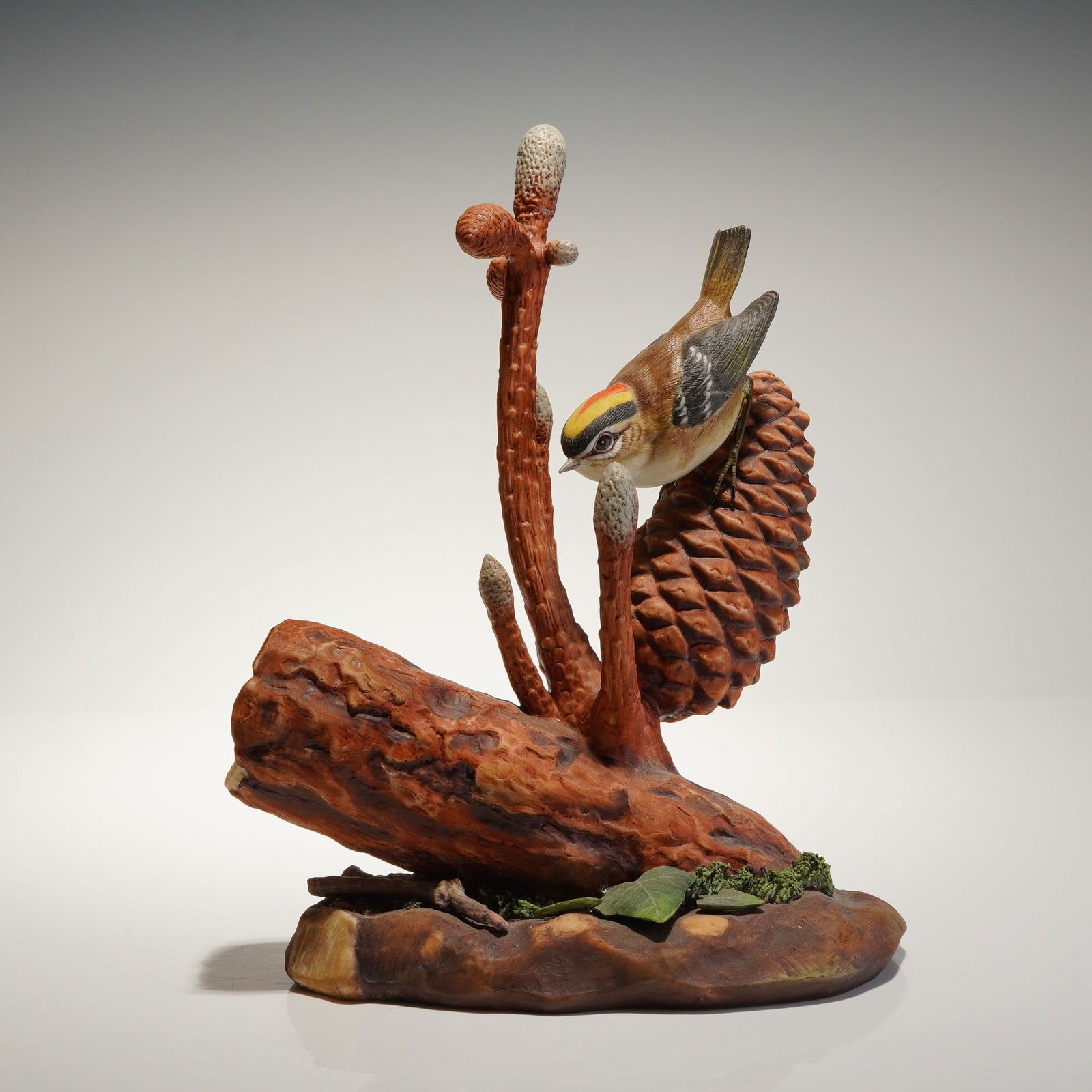 Royal Doulton Figurine Golden-Crowned Kinglet HN3504: A single naturalistic polychrome painted porcelain figurine depicting a Golden-Crowned Kinglet Regulus satrapa satrapa perched on a large pine cone, which is attached to a rough, broken log base detai