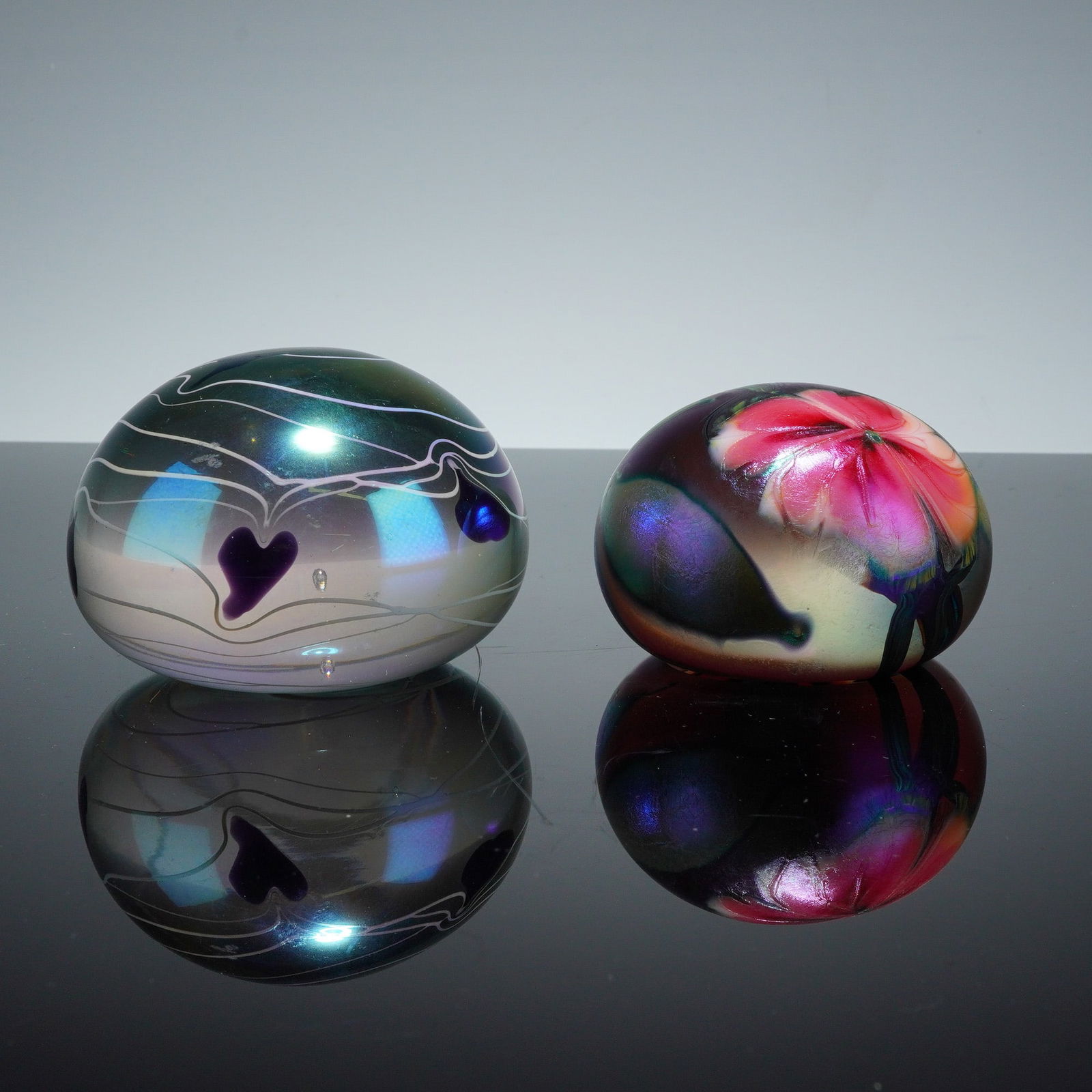 2pc David Lotton Dua Flora & After Robert Eickholt Hearts Vine Paperweights: The first example is the "Dua Flora" pattern by American glass artist David Lotton, featuring vibrant pink multi-petaled blossoms with green foliage against a dark, metallic iridescent ground. The und