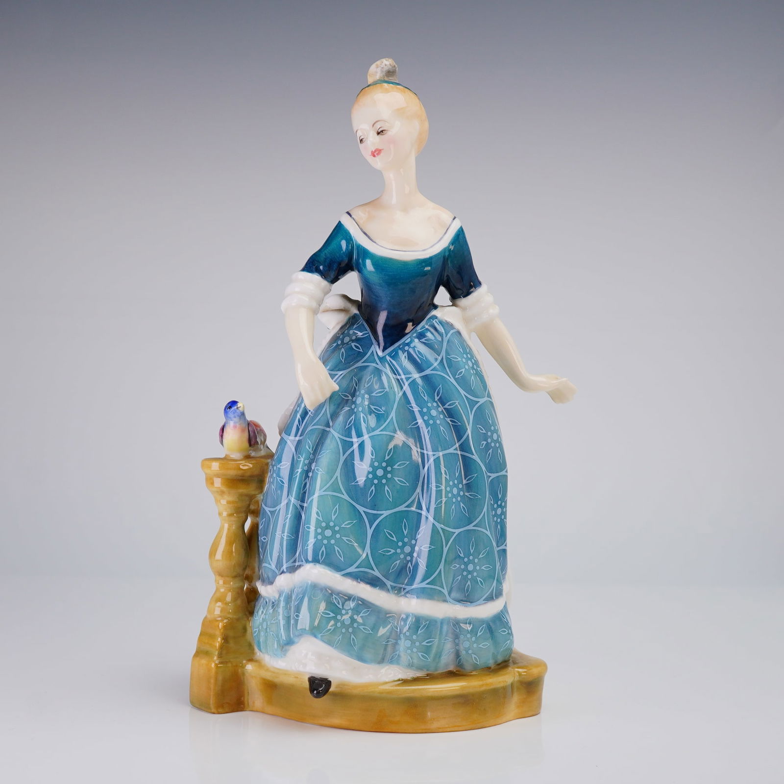 Royal Doulton Clarinda HN2724 Bone China Figurine: Royal Doulton Bone China Figurine, Clarinda (HN2724), depicting a woman in a blue patterned dress standing next to a yellow balustrade with a bird, marked 1974 on the base. Dimensions: 5.00"L x 4.00"W