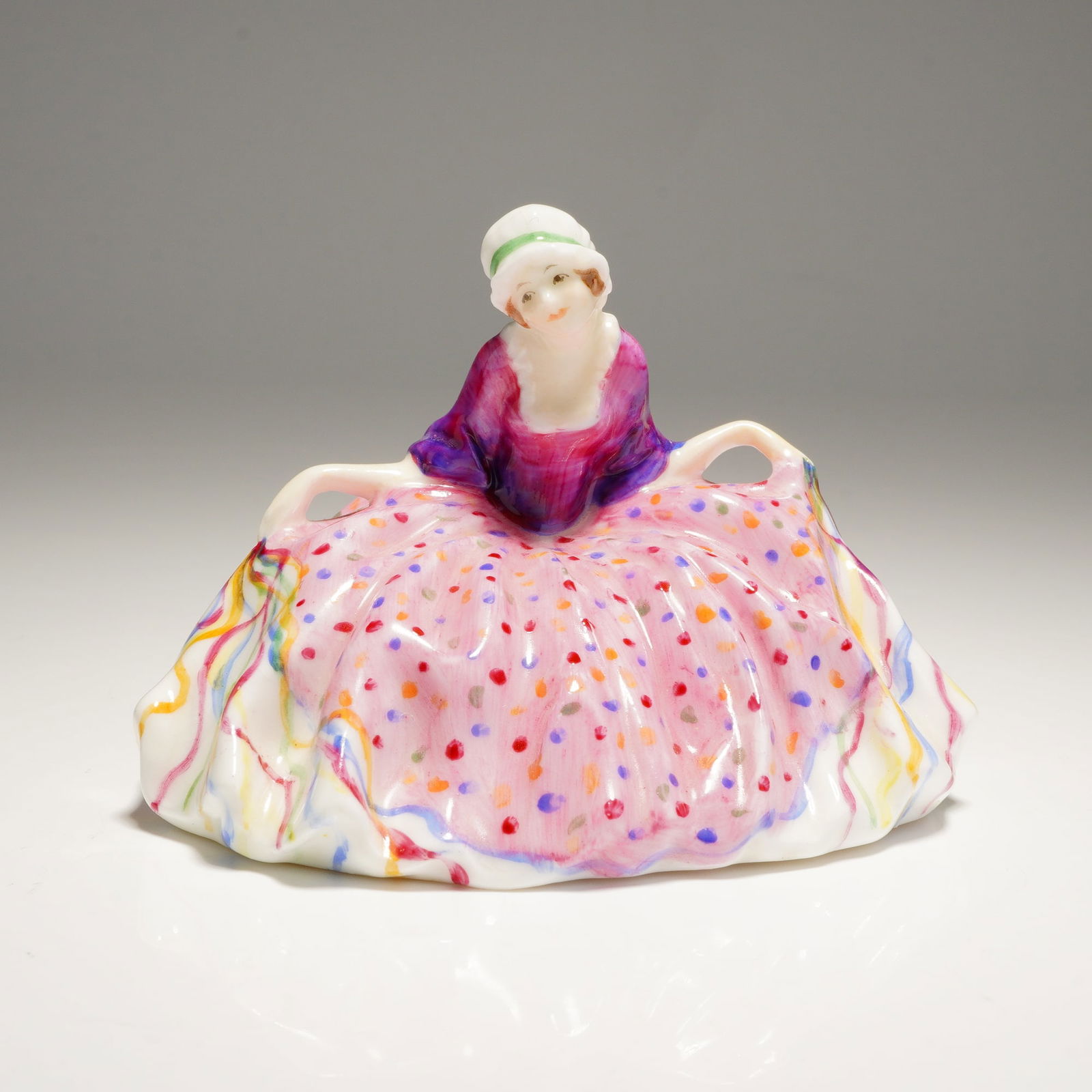 Royal Doulton Miniature Figurine Polly Peachum M23: A single ceramic figurine of a seated woman in white, pink, purple, and multicolored attire, marked Polly Peachum, M.23., G.W., and ROYAL DOULTON ENGLAND. Dimensions: 3.25"L x 2.50"W x 2.25"H Weight: