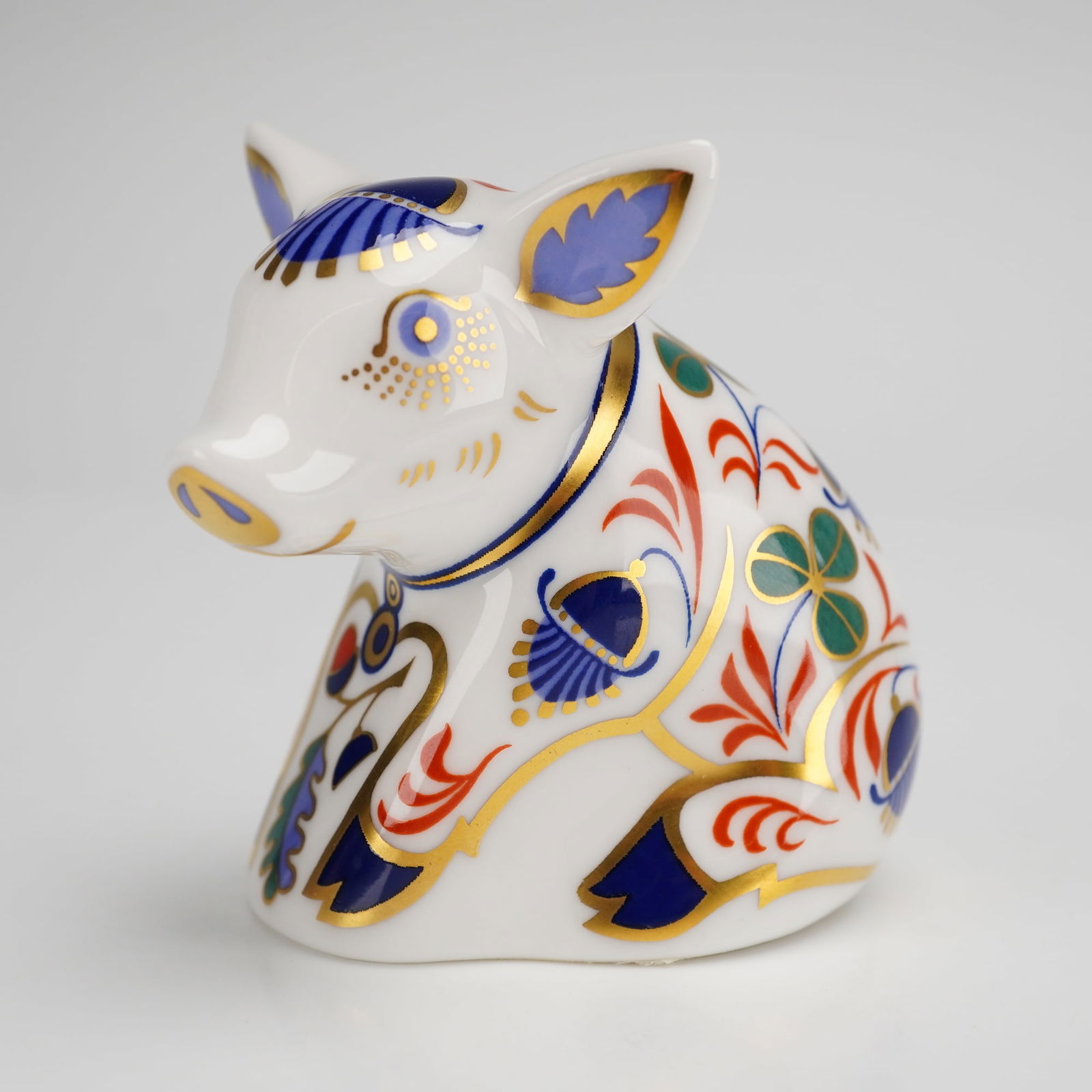 Royal Crown Derby Sitting Piglet Bone China Paperweight: A Royal Crown Derby fine bone china paperweight in the form of a Sitting Piglet. The figurine is decorated in a traditional Imari-style pattern with floral and foliate motifs in cobalt blue, iron red,