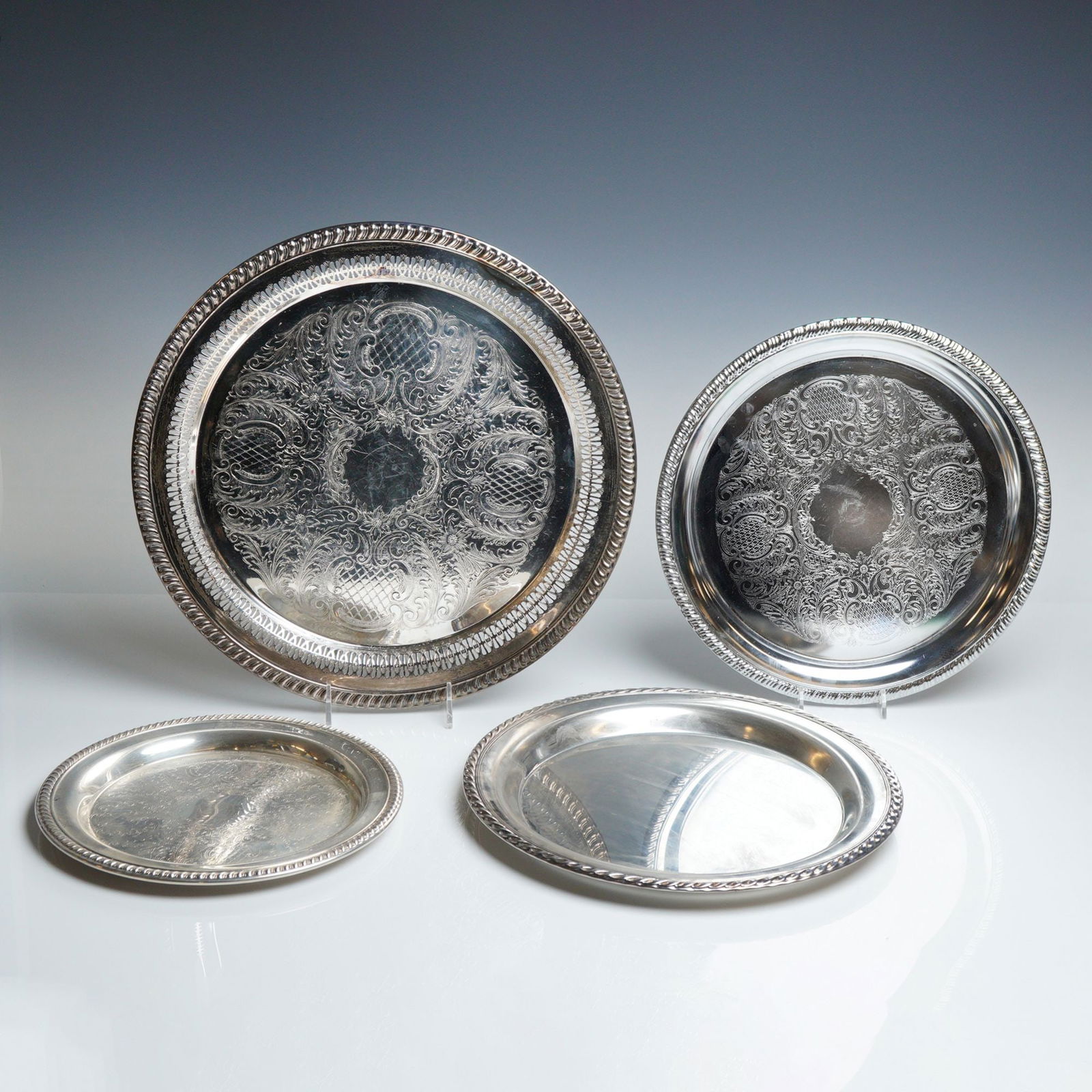 4pc Wm. Rogers, Sheridan & Leonard Silverplated Serving Trays: The group consists of circular platters in varying sizes, featuring traditional mid-20th-century design elements. Decorative motifs include intricate etched foliate and lattice patterns on two of the