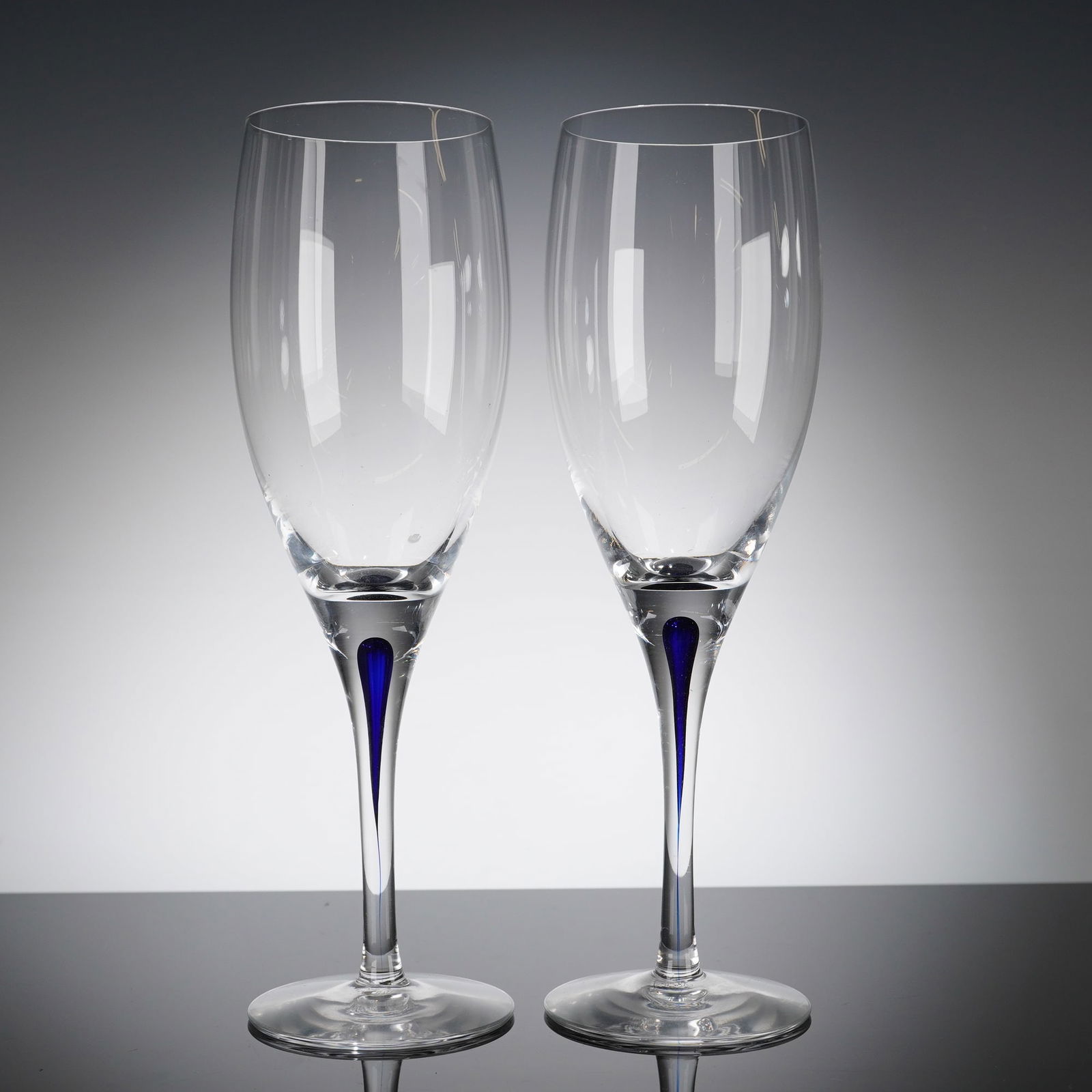 A Pair of Orrefors Intermezzo Blue Crystal Champagne Flutes: A pair of Orrefors Crystal Intermezzo Blue glasses, identified as sparkling wine glasses or champagne fi?utes. Each glass is crafted from clear colorless crystal featuring a tall, tapering bowl. The