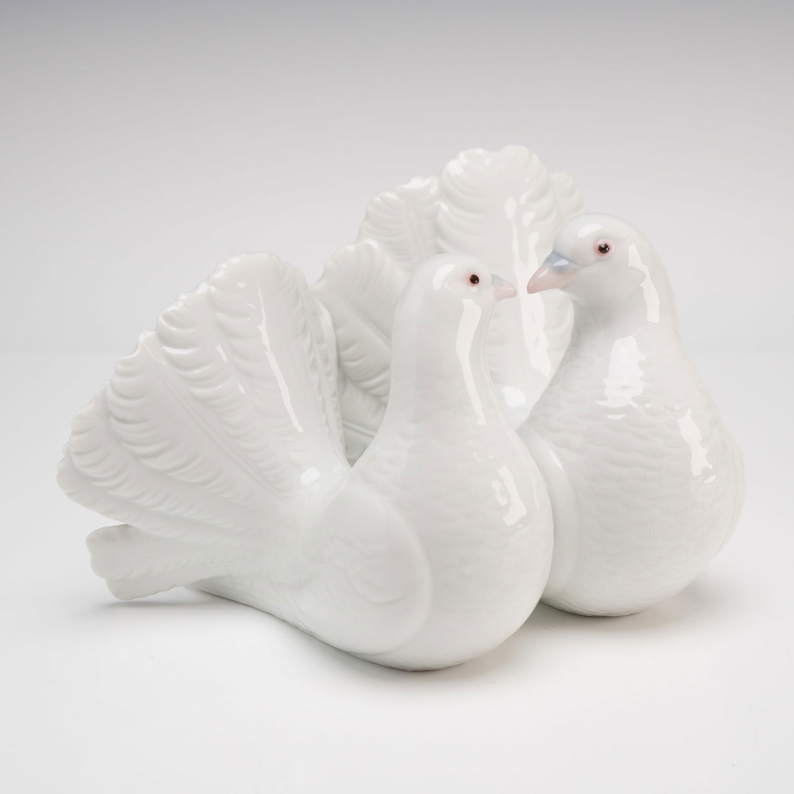 Lladro Couple of Doves Porcelain Figurine, Model 1169: This fine glazed porcelain figurine by Lladro, titled Couple of Doves, depicts a pair of white fantail birds in a courting pose with their distinctive fan-shaped tail plumage prominently displayed.