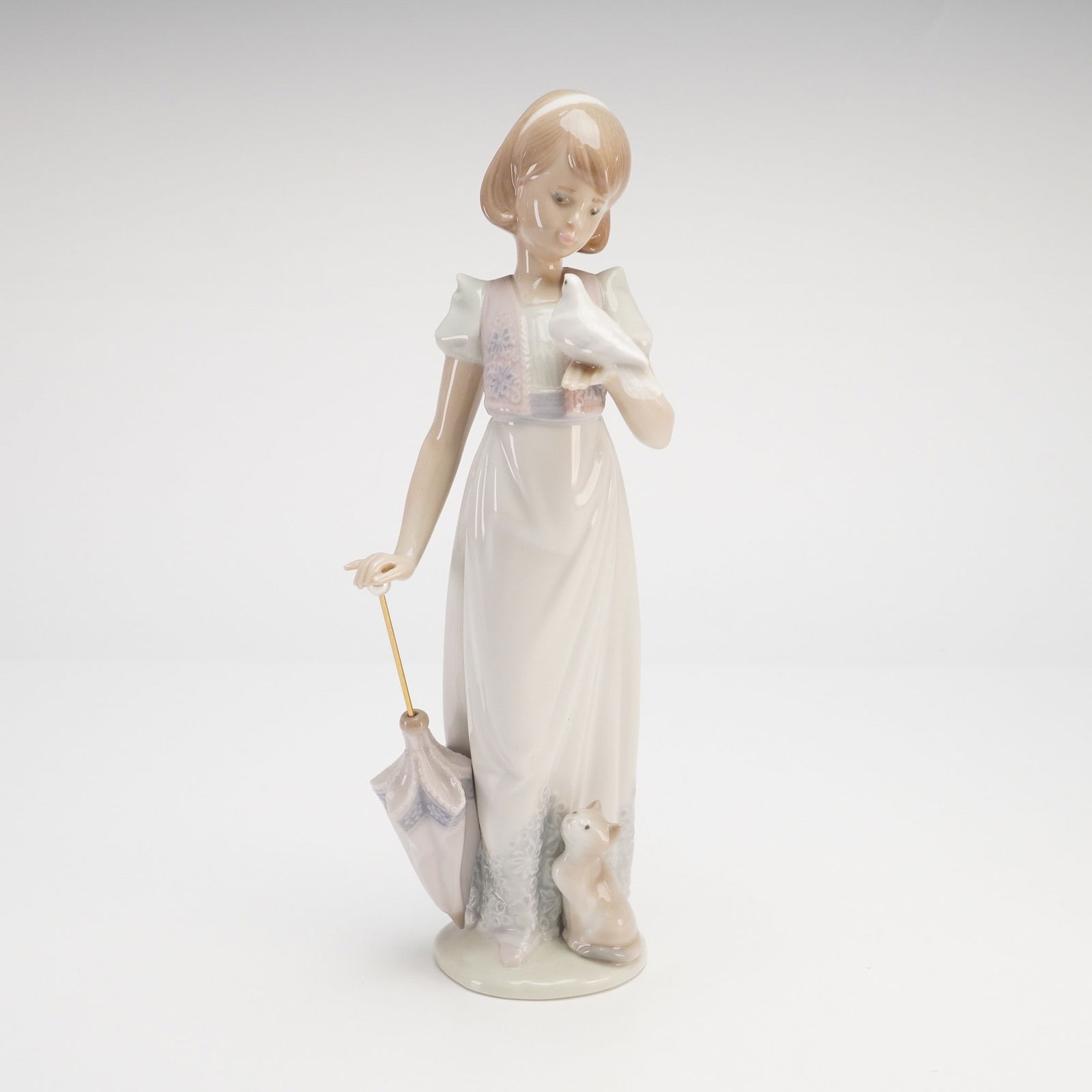 Lladro Summer Stroll Figurine, Model 7611: This Lladro glossy figurine model 7611, titled Summer Stroll, depicts a slender young girl in a graceful, full-length pale cream dress with lavender-blue floral accents on the bodice and lower hem.