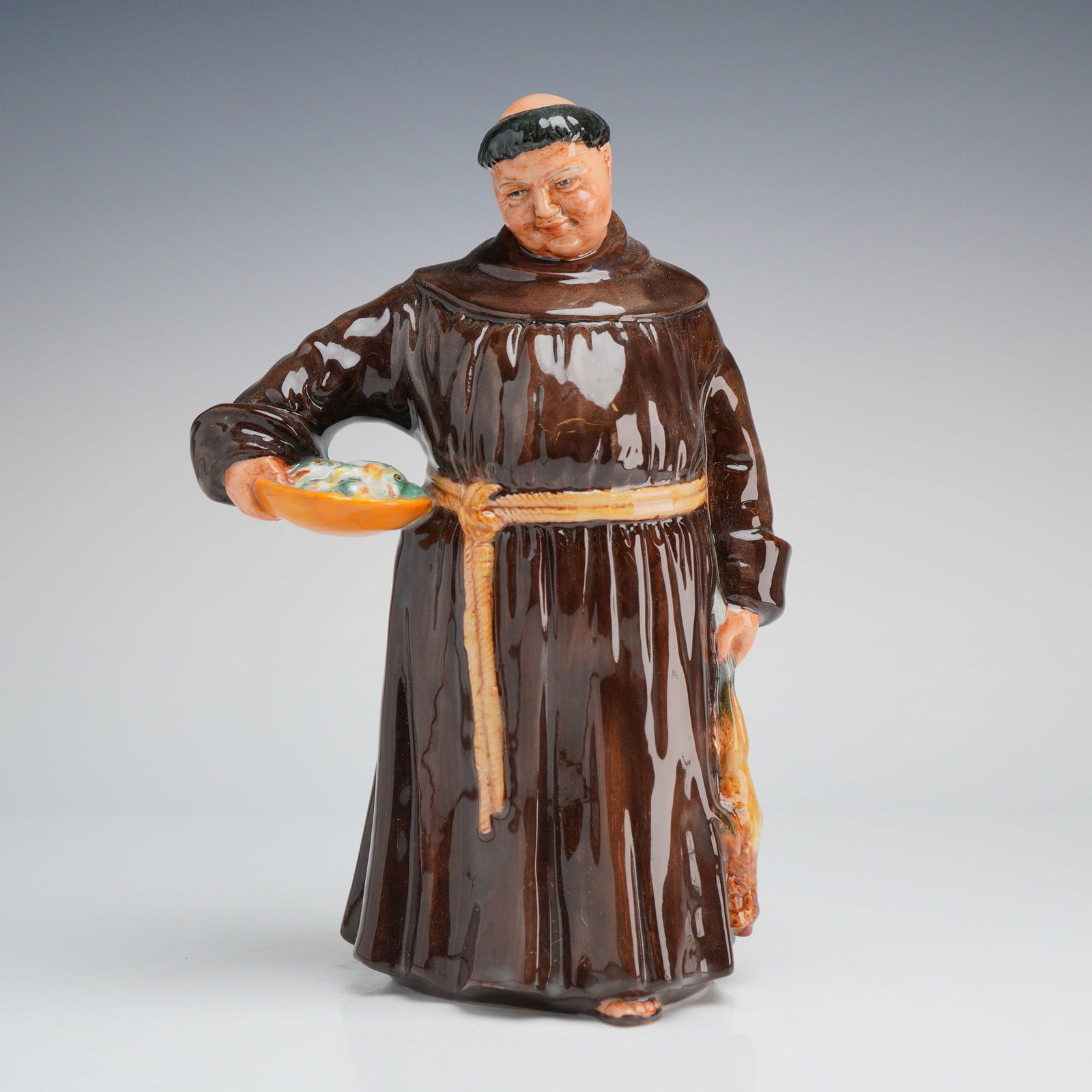 Royal Doulton Figurine, Jovial Monk HN 2144: A Royal Doulton glazed ceramic figurine titled The Jovial Monk, model number HN 2144. The figure is depicted in a traditional brown habit with a yellow cord belt, carrying a shallow bowl of fish in hi