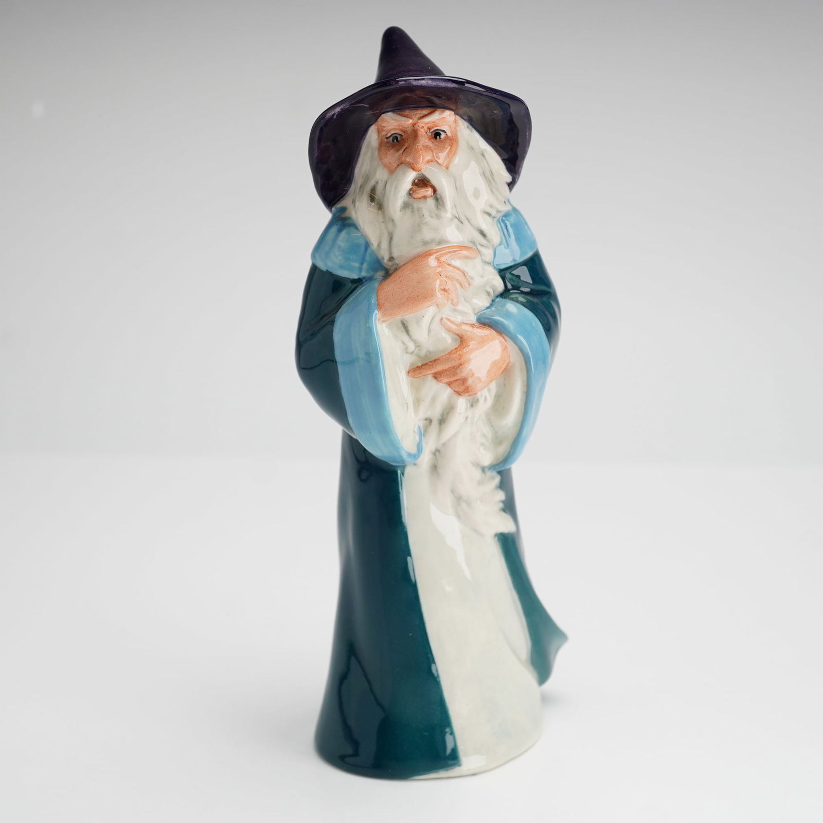 Royal Doulton Middle Earth Lord of the Rings Figurine, Gandalf HN2911: This Royal Doulton figurine, titled Gandalf (HN 2911), is part of the Middle Earth series. The glazed ceramic figure is modeled in a standing pose, wearing layered navy and light blue robes with a poi