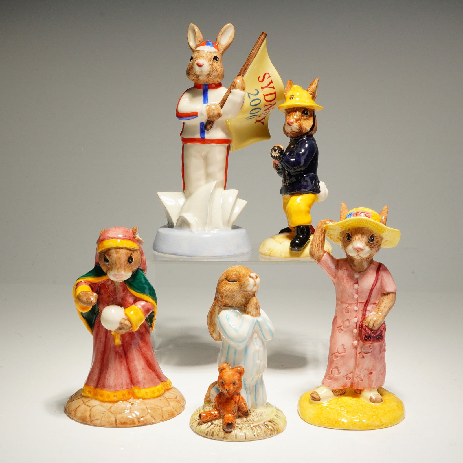 5pc Royal Doulton Bunnykins Figurines: A 5pc collection of Royal Doulton Bunnykins glazed ceramic figurines featuring various rabbit characters in thematic costumes. The group includes England Athlete Sydney 2000 DB 216 in a track suit wit