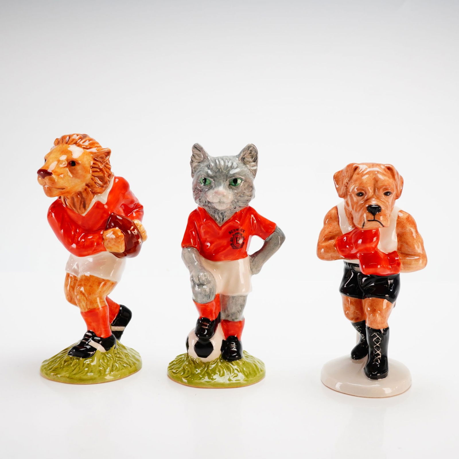 Beswick Sporting Character and Footballing Felines Figurines: This professional set of 3pc Beswick figurines including Sporting Character Collection-Last Lion of Defense and It's a Knockout and from Footballing Felines-Kitcat was manufactured in England in 1998.