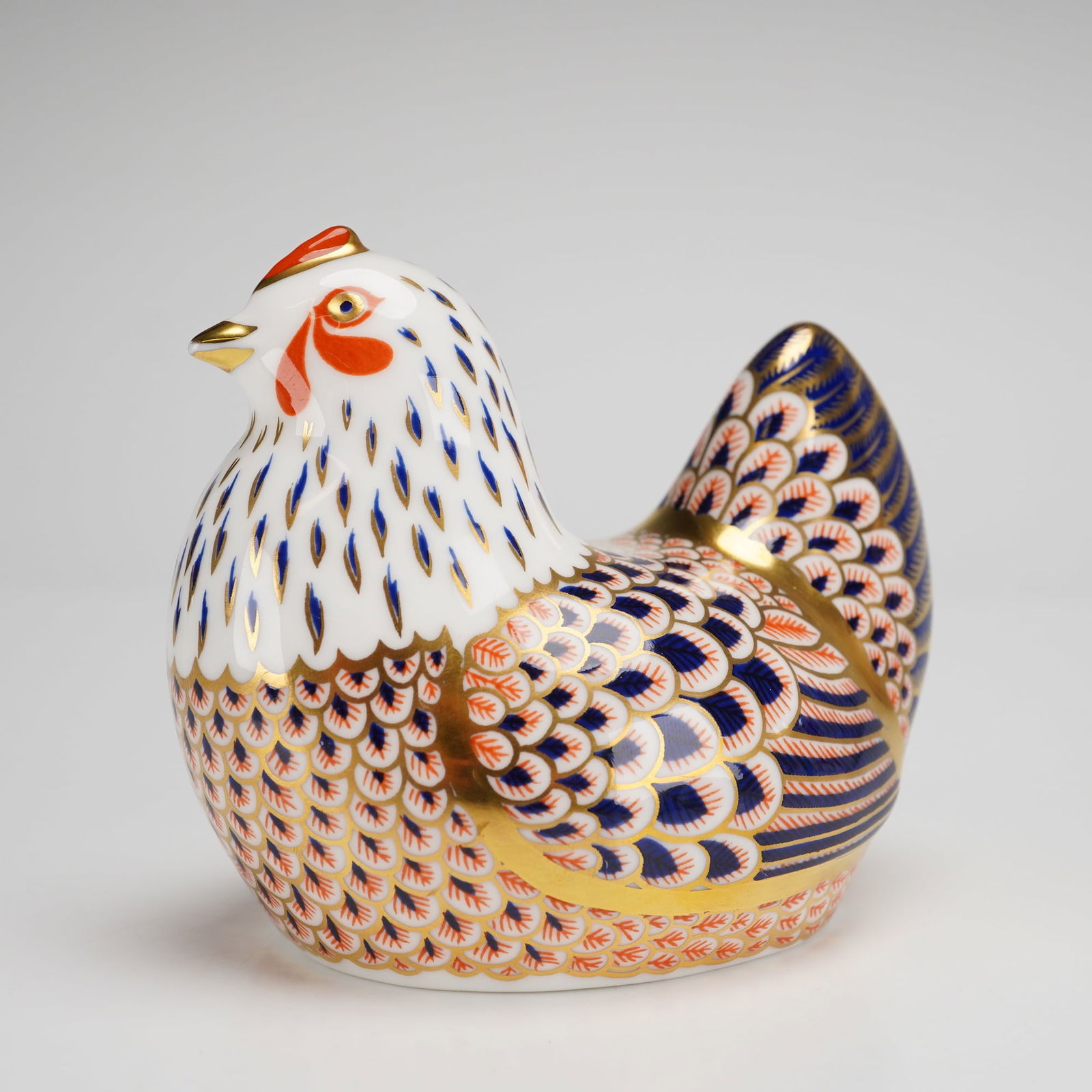 Royal Crown Derby Bone China Paperweight Chicken: A Royal Crown Derby fine bone china paperweight modeled as a chicken, decorated in a traditional Imari-style palette of cobalt blue, iron red, and 22ct gold gilding. The figurine features intricate