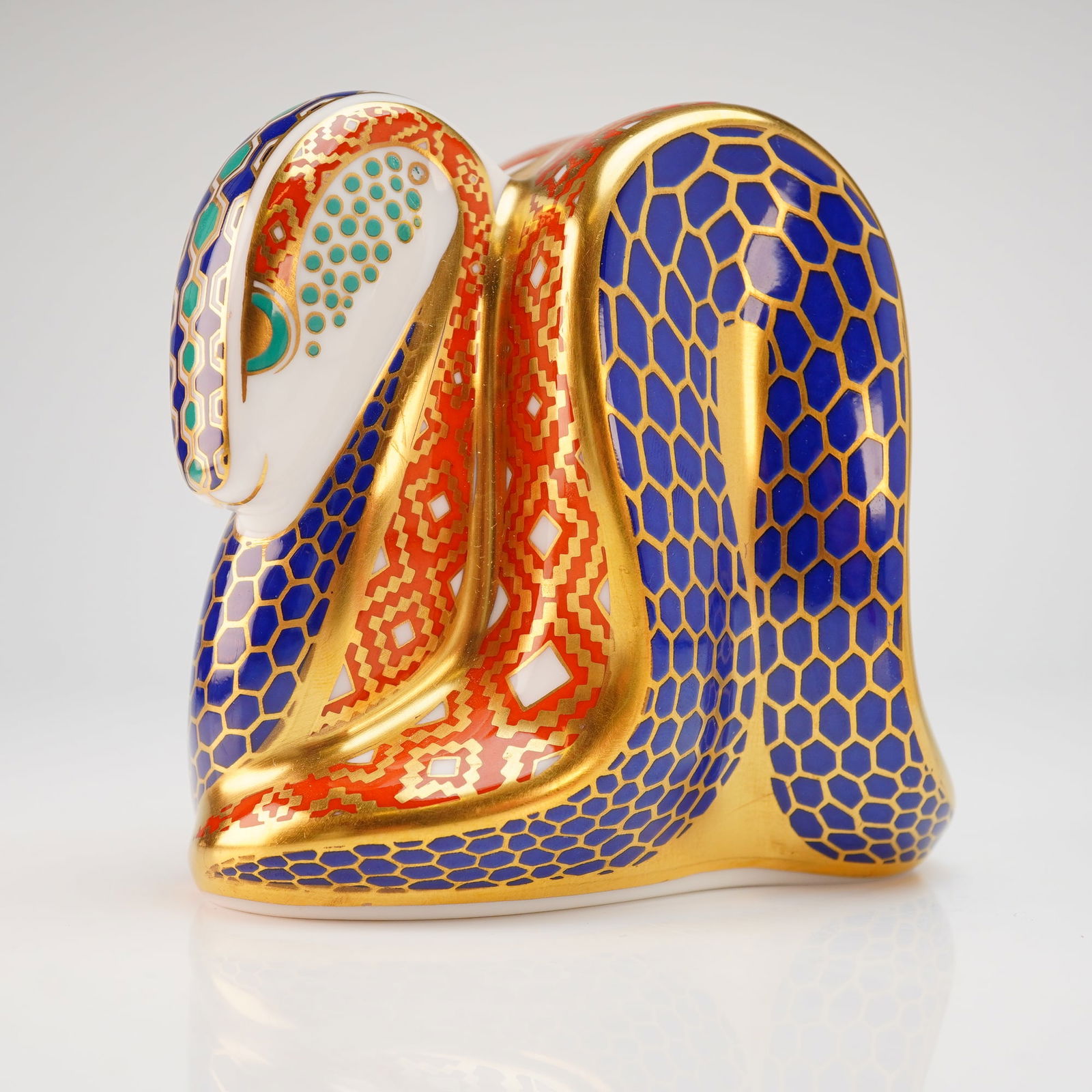 Royal Crown Derby Old Imari Snake Paperweight: A Royal Crown Derby bone china paperweight modeled as a coiled snake and decorated in the Old Imari pattern. The design features a cobalt blue honeycomb scale motif and a geometric diamond pattern in