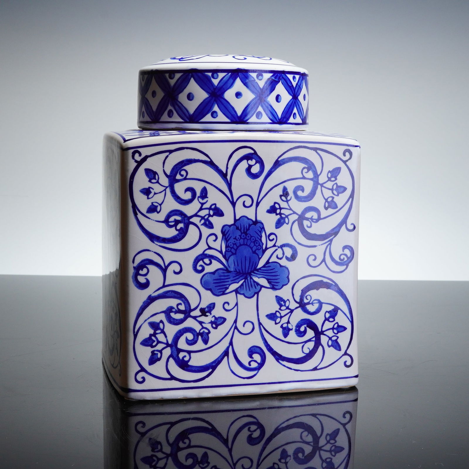 Bombay Blue Floral Swirl Square Ceramic Ginger Jar with Lid: A blue and white square-form ceramic jar and fitted lid decorated in a Bombay blue floral swirl pattern. The body is decorated with dense, flowing foliate scrolls surrounding a centralized stylized fl