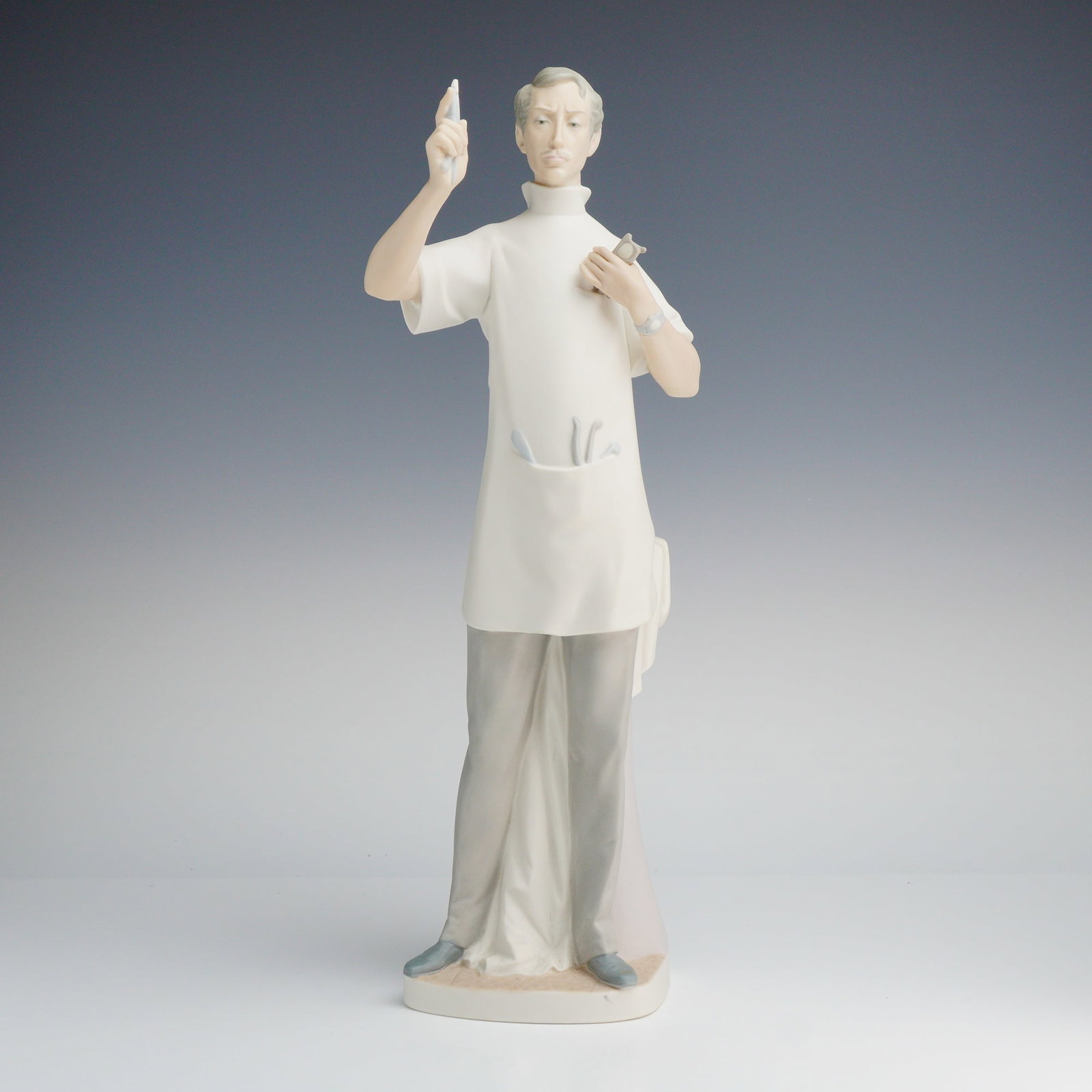 Lladro Dentist Matte Finish Porcelain Figurine 1014762: A Lladro porcelain figurine titled Dentist, model number 1014762, featuring a matte finish. The figure depicts a male dentist in a professional smock and trousers. He holds dental instruments in each