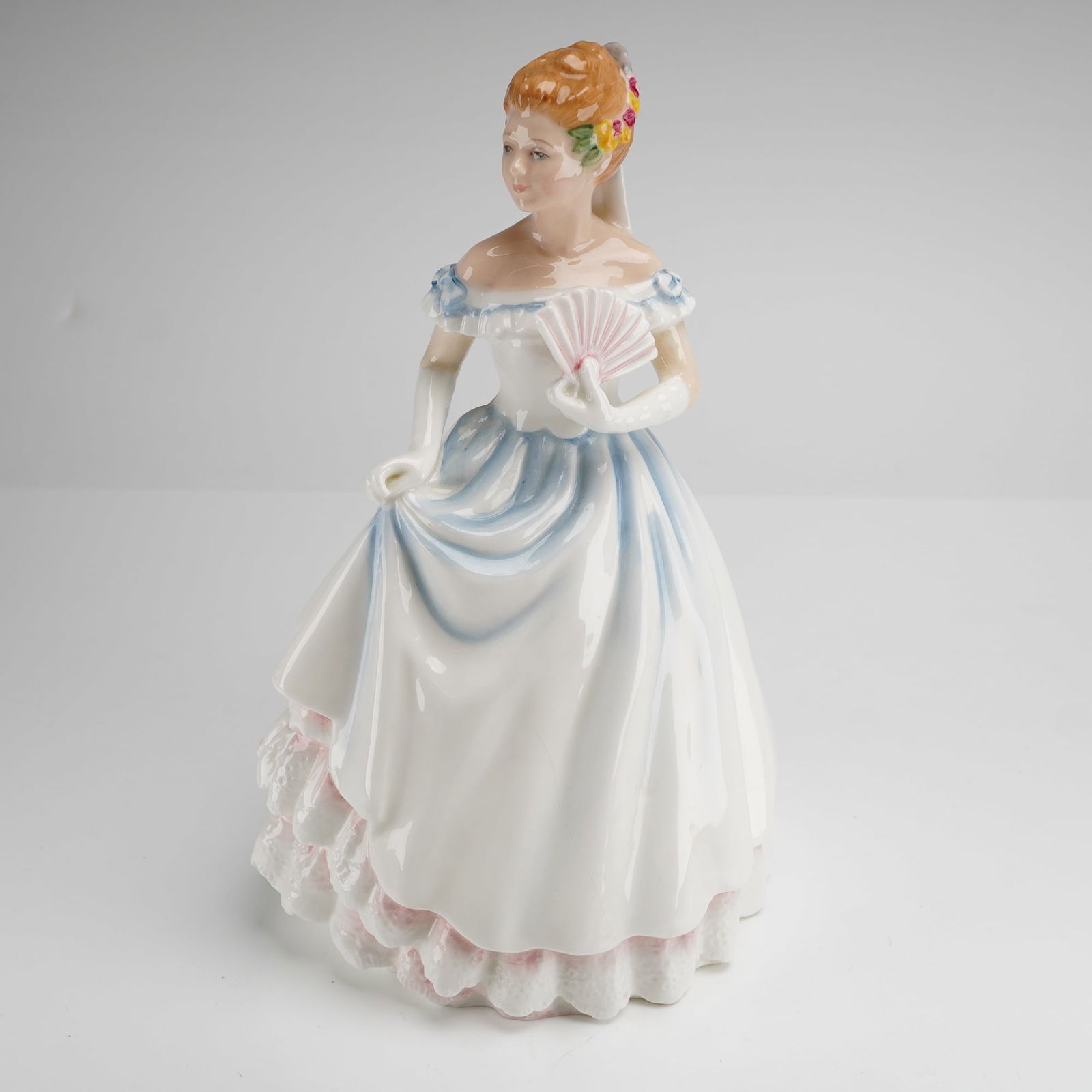 Royal Doulton Claire HN 3646 Bone China Figurine: A Royal Doulton hand-decorated bone china figurine titled Claire, model number HN 3646. The figure is depicted in a formal white gown featuring light blue and pink accents, holding a fan with floral o