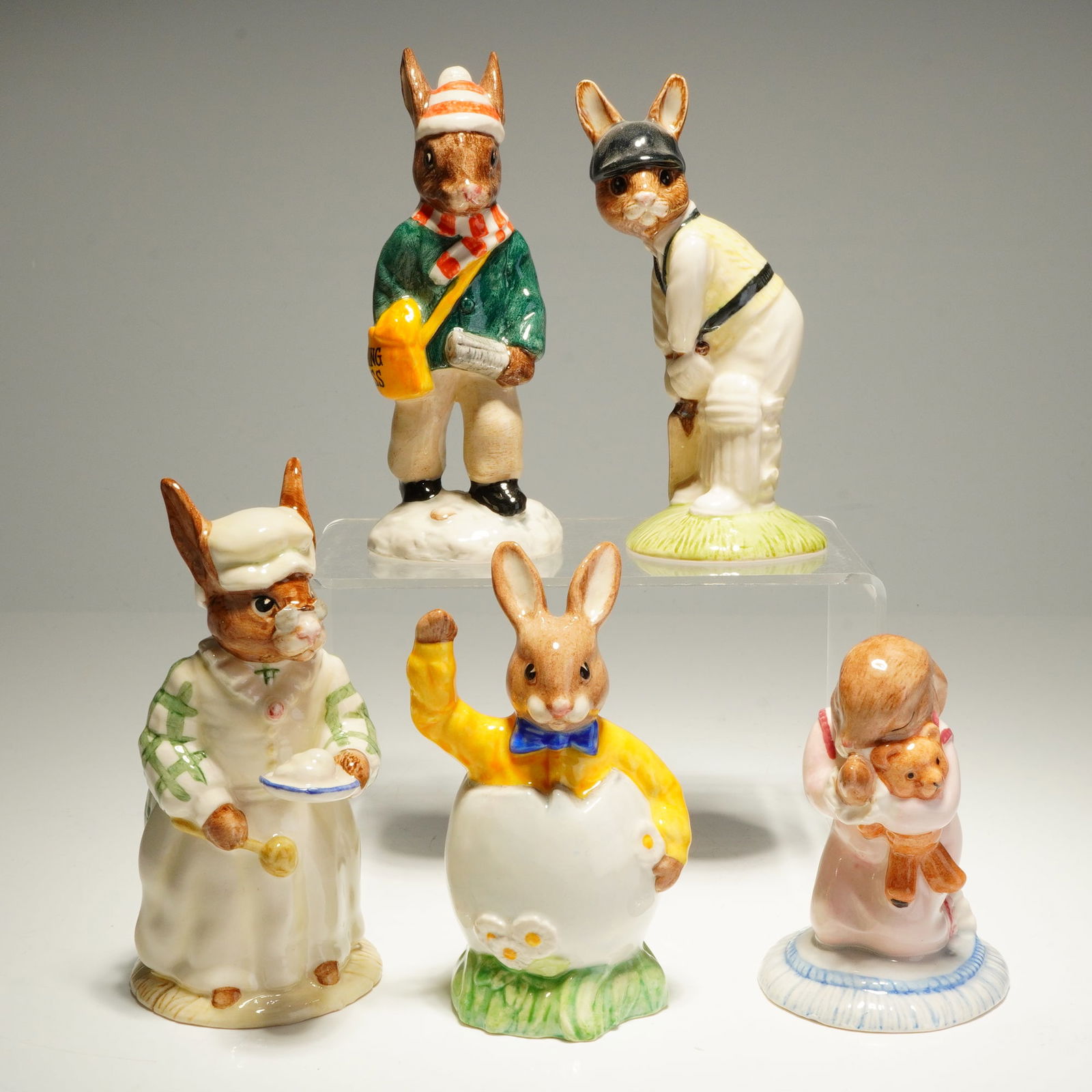 Collection of Five Royal Doulton Bunnykins Batsman Cook Goodnight Paperboy: This collection of five Royal Doulton Bunnykins figurines features anthropomorphic rabbits in various thematic roles. The group includes Batsman Bunnykins DB144, depicted as a cricket player in tradit