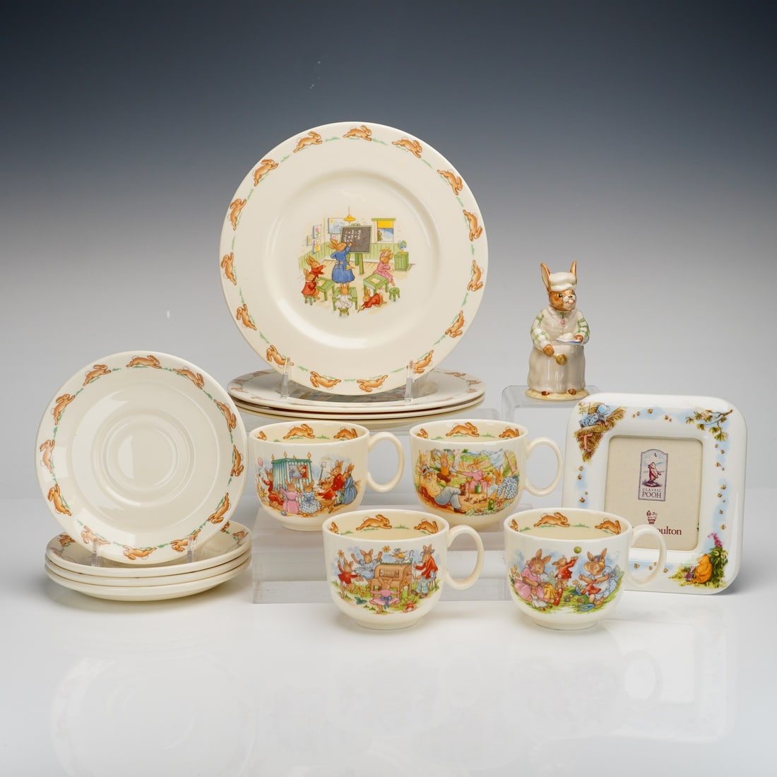 14pc Royal Doulton Bunnykins Ceramic Nursery Ware , Figurine & Frame: A 14pc Royal Doulton Bunnykins set including four plates, four cup and saucer sets, a figurine, and a frame. The nursery ware is constructed of bone china and features various transfer-printed illustr