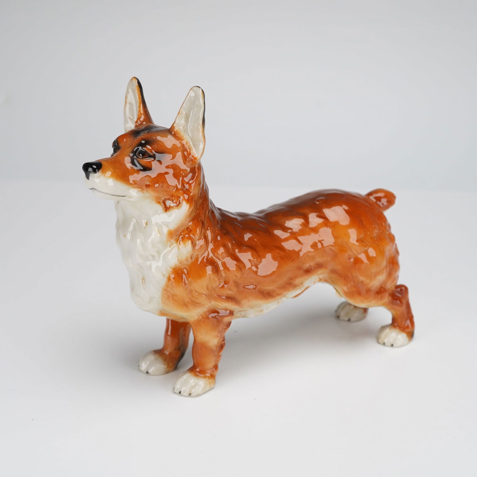 Goebel Porcelain Welsh Corgi Dog Figurine: A glazed ceramic figural sculpture by Goebel, depicting a Welsh Corgi standing alertly. The figure is finished with a high-gloss glaze, utilizing reddish-brown and tan coloring for the coat, contraste