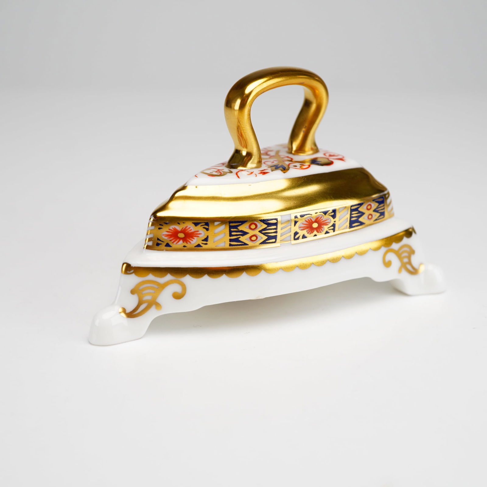 Royal Crown Derby Porcelain Imari Figurine, Iron on Stand: The piece is modeled as a traditional flatiron resting on a scrolled tripod base. The decoration follows the traditional Imari pattern with a palette of iron-red, cobalt blue, and gold gilding, featur