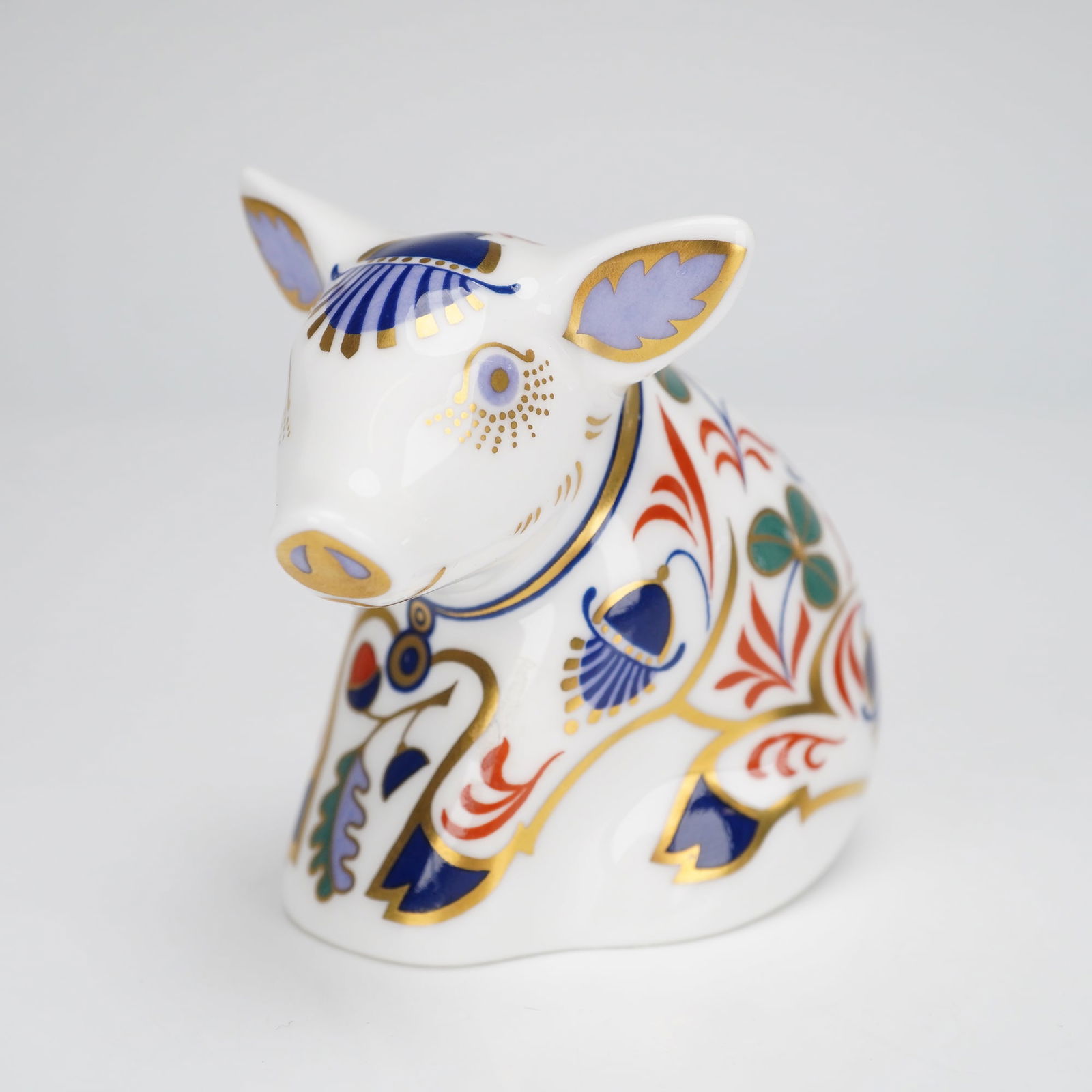Royal Crown Derby Sitting Piglet Paperweight: A Royal Crown Derby bone china paperweight, titled Sitting Piglet. The figurine is executed in white glazed porcelain and is decorated in the traditional Imari palette, featuring stylized floral and f