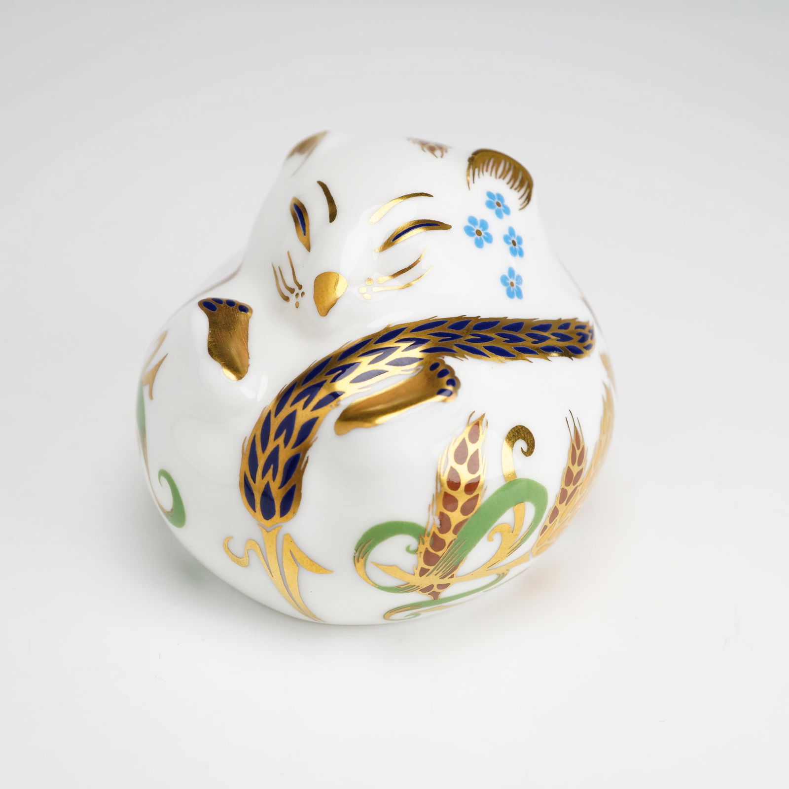 Royal Crown Derby Dormouse Paperweight: This Royal Crown Derby English bone china paperweight is modeled as a sleeping dormouse in a curled pose. The figurine is decorated with patterns of wheat ears, small blue flowers, and scrolling folia