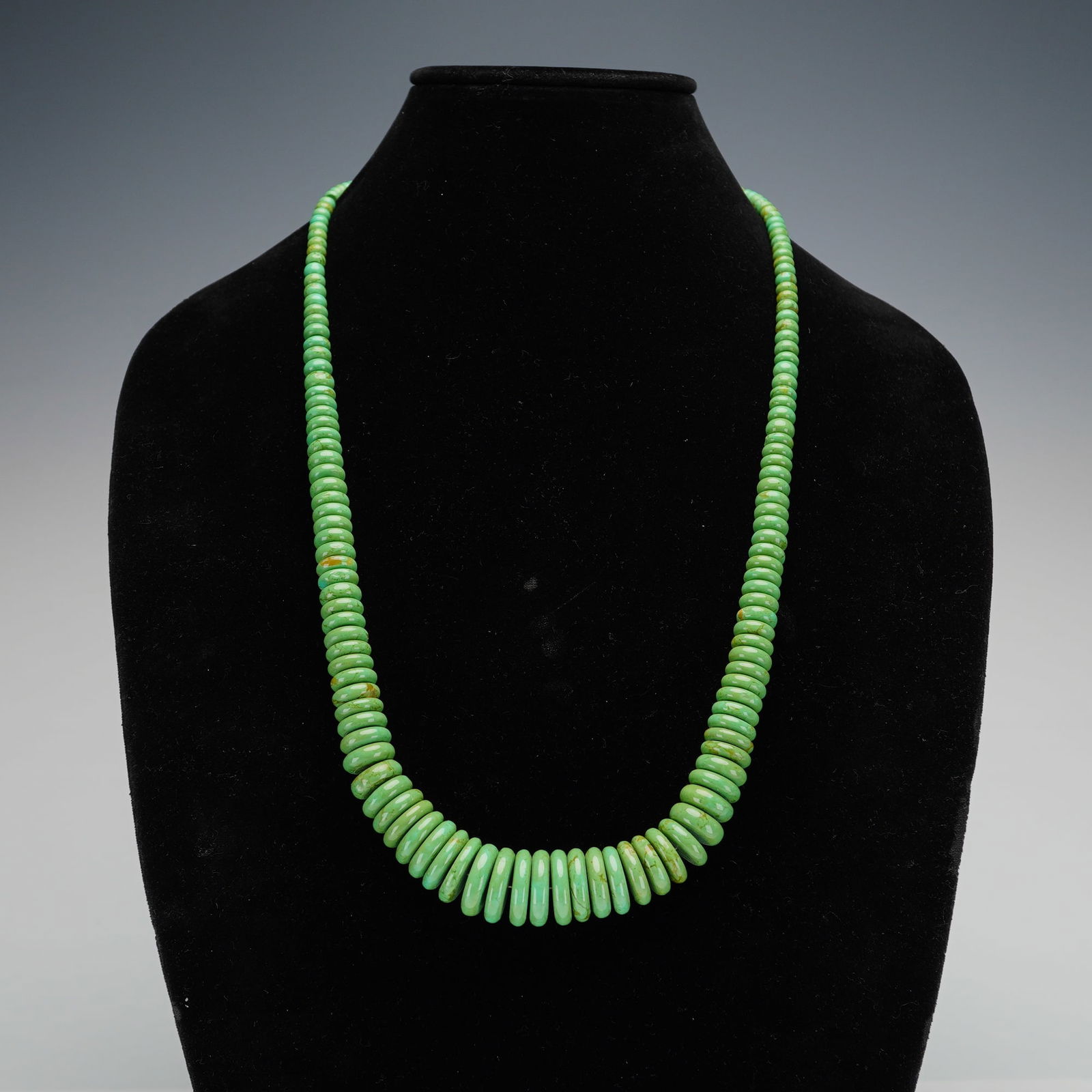 Graduated Green Turquoise and Sterling Silver Necklace: A green stone necklace with sterling fasteners featuring a single strand of graduated green turquoise rondelle beads. The beads display natural matrix variations in shades of yellow and brown. The str