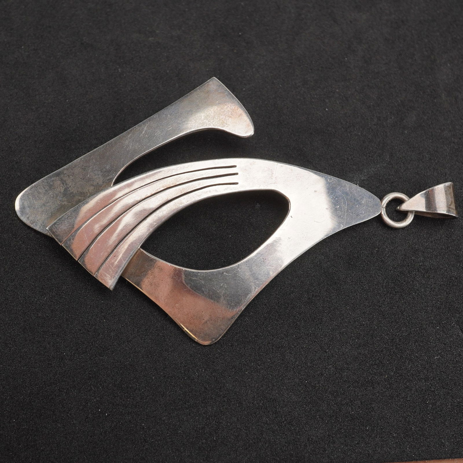Mexican Sterling Silver Abstract Design Pendant: A Modernist pendant crafted from sterling silver, featuring an abstract, geometric design composed of layered, curved planes. The highly polished surfaces are accented by four parallel incised lines f