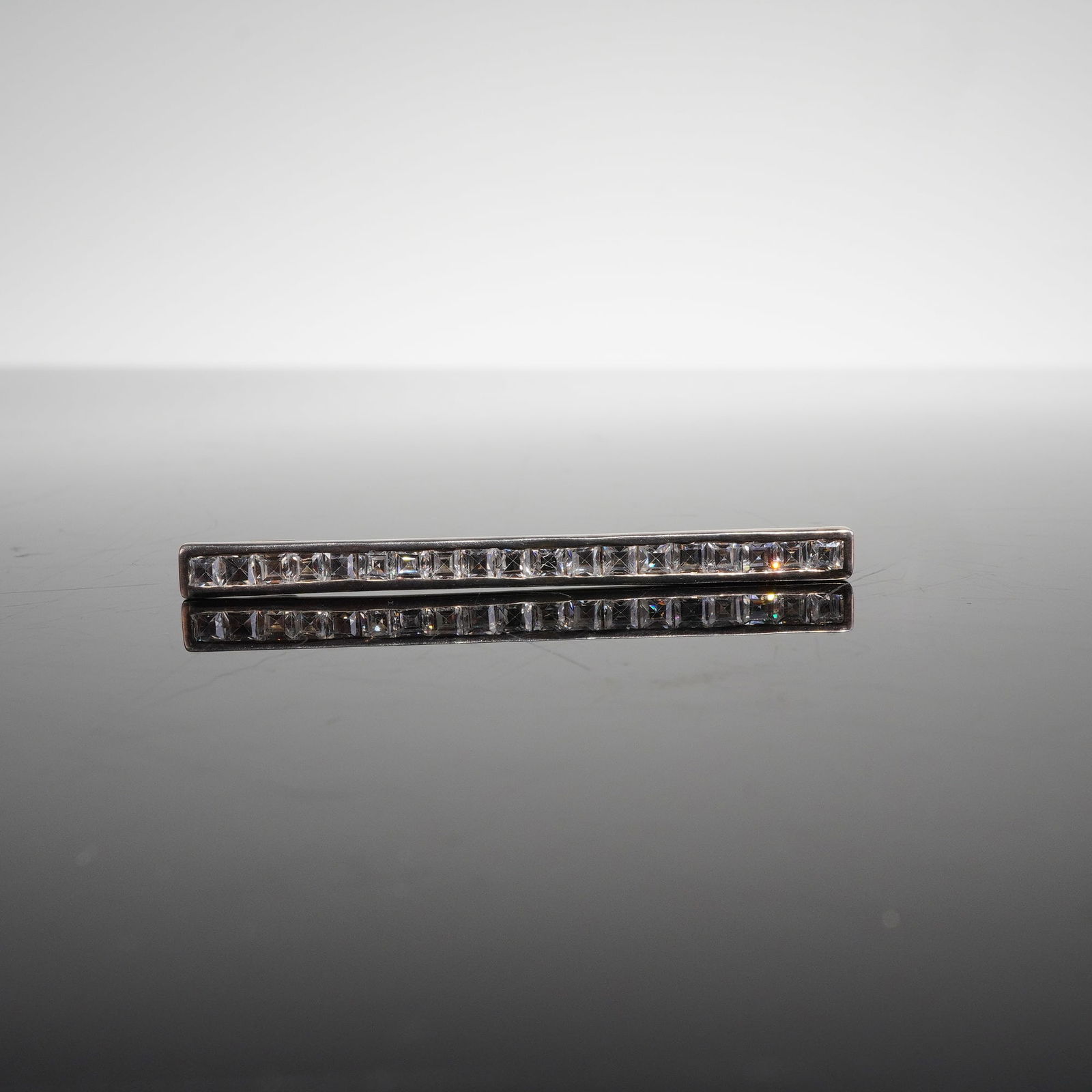 Art Deco Style Sterling Silver Bar Brooch with CZ Stones: A single sterling silver pin executed in a streamlined, geometric Art Deco style. The bar brooch features two parallel rows of closely aligned, square-cut colorless stones, which are identified as whi