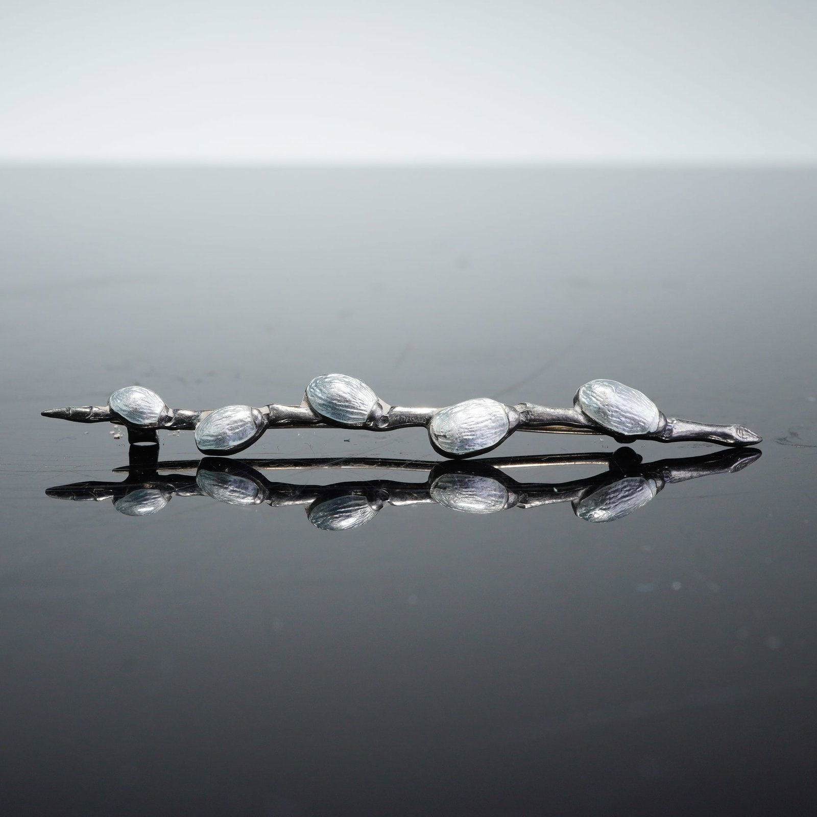 Sterling Silver and Enamel Buds on a Branch Brooch: A sterling silver brooch designed in the form of a budding branch, featuring five raised oval elements. The piece is constructed with a naturalistic, textured silver stem. Each element is finished wit