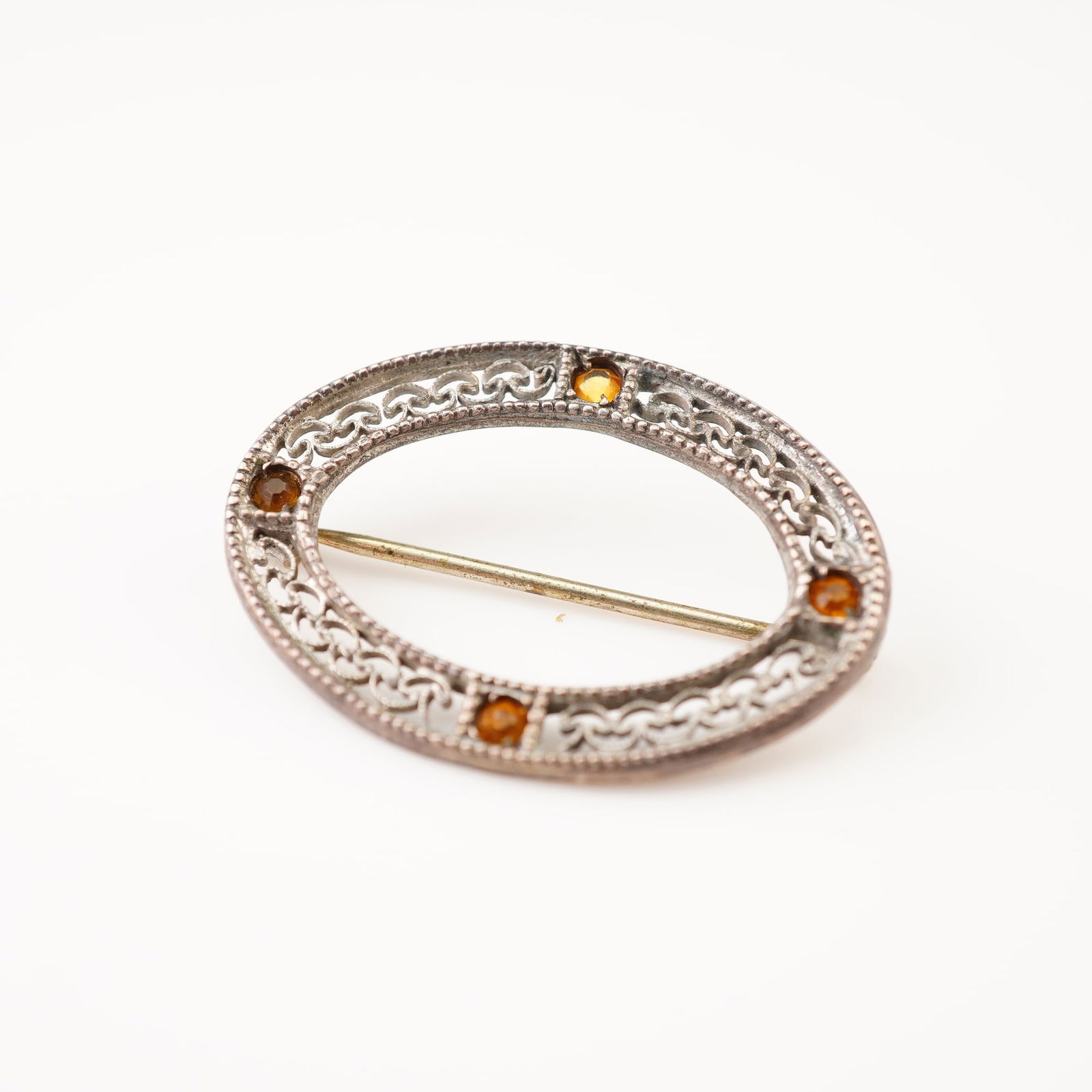 Sterling Silver Oval Openwork Brooch with Amber-Toned Stones: This vintage oval brooch is crafted from sterling silver and features an intricate scrolling openwork interior. The frame is finished with a milgrain beaded border on both the inner and outer edges. T