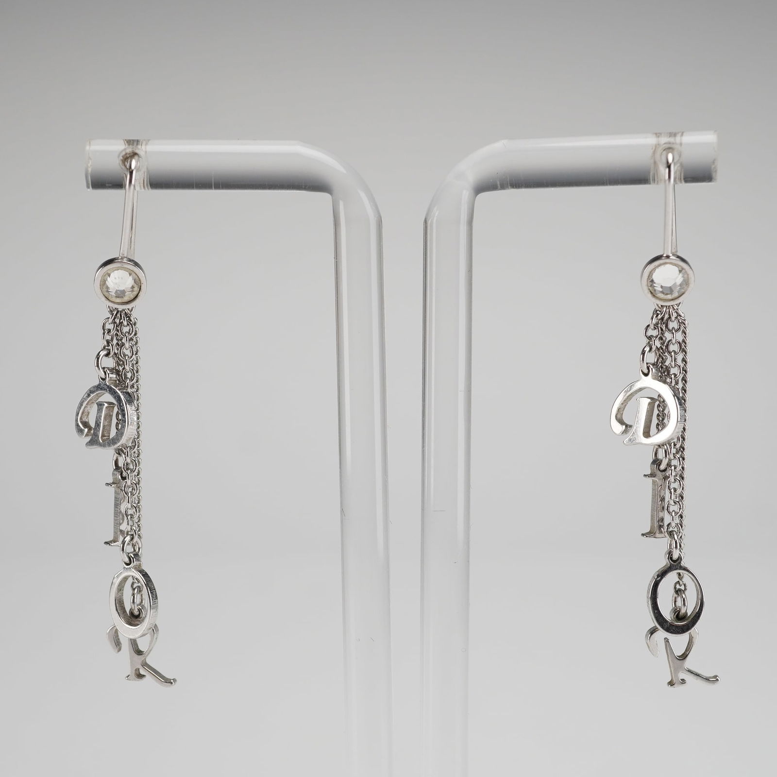 A Pair of Vintage Christian Dior Logo Dangle Earrings: A pair of vintage Christian Dior dangle earrings constructed of silver-toned base metal. Each earring utilizes a fish hook wire attachment above a bezel-set, colorless faceted stone, likely paste or